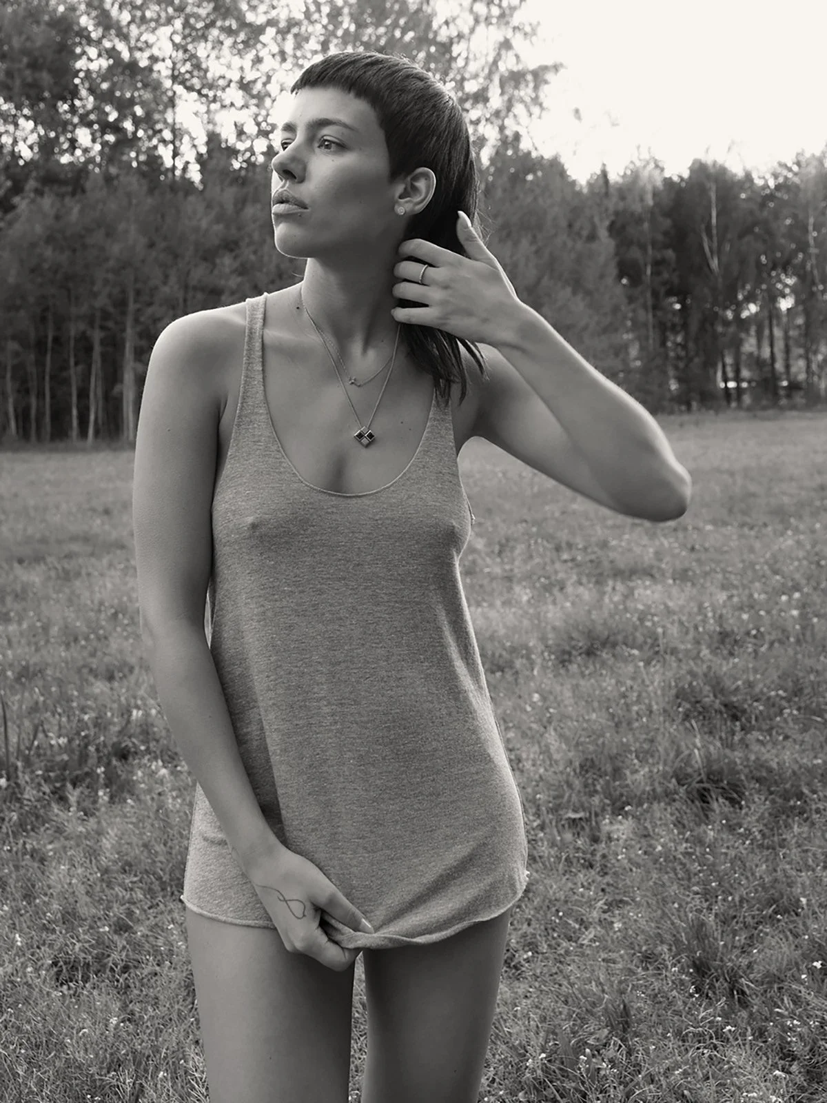 Black and white photo of a person in a tank top standing in a grassy field with trees in the background.