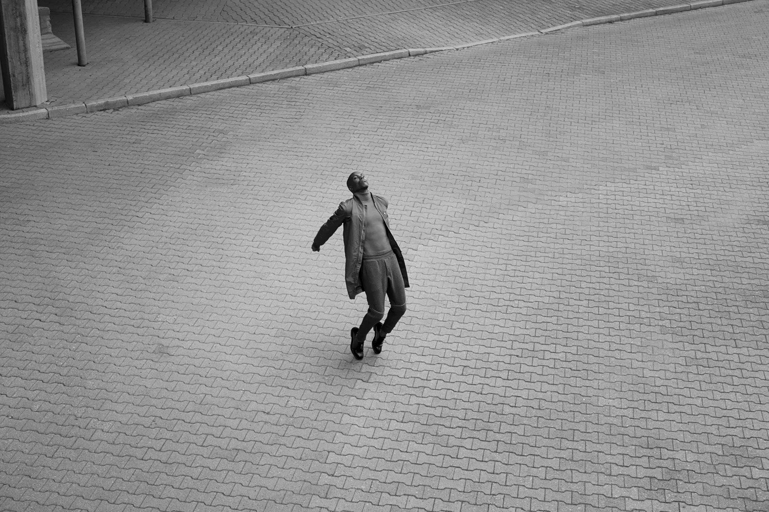 Person in dark clothing walking or dancing on a paved surface in a black and white image.