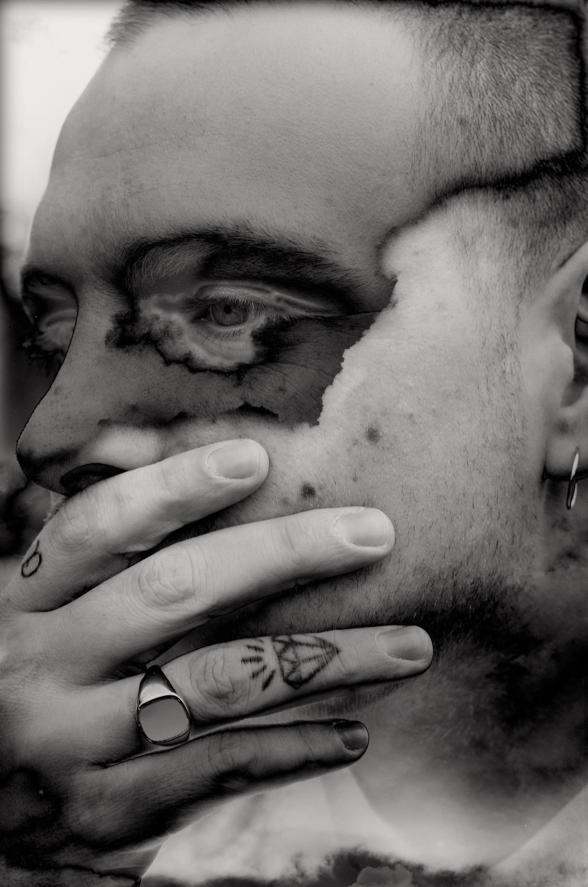 Surreal black and white portrait of a person with a hand partially covering their face, featuring tattoos, rings, and a distorted texture overlay.