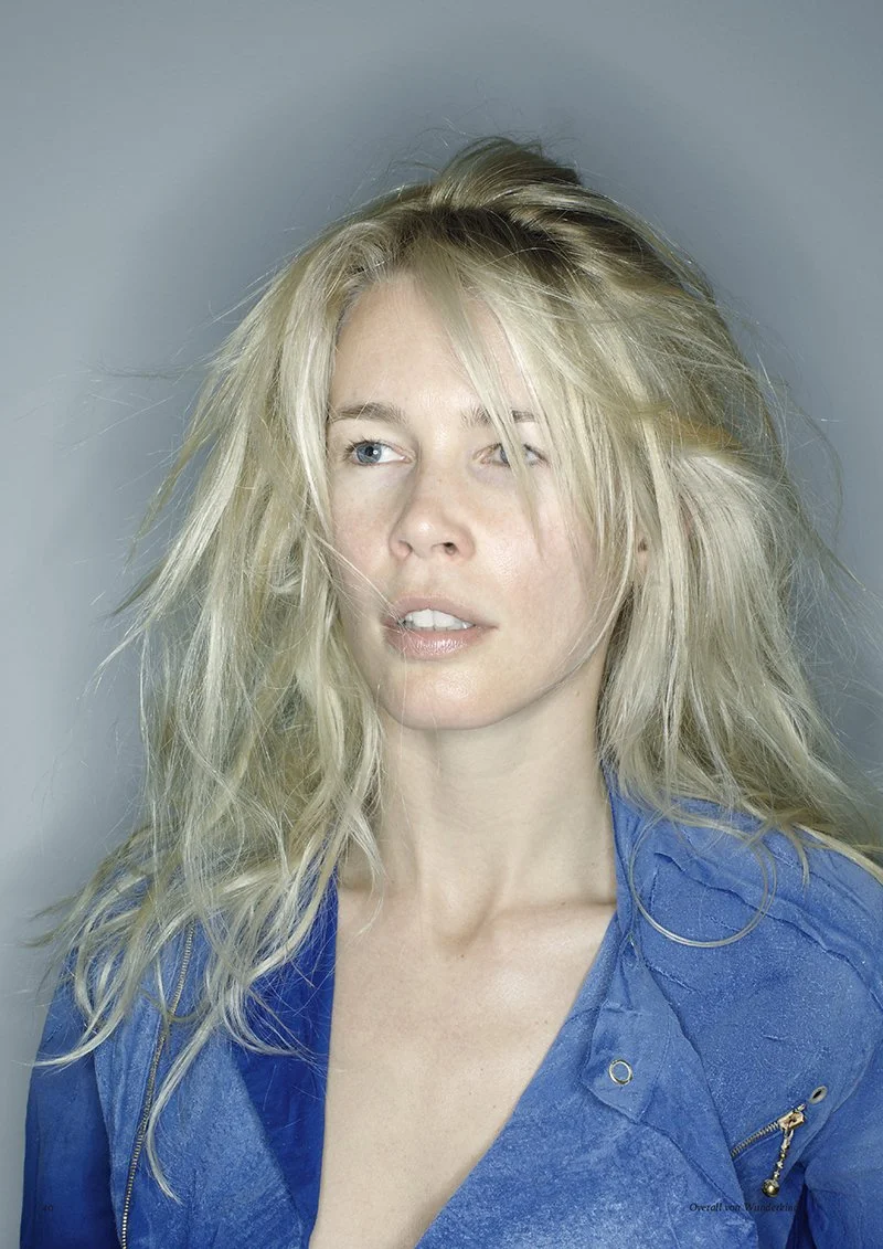 Woman with long blonde hair wearing a blue jacket, looking slightly to the side.