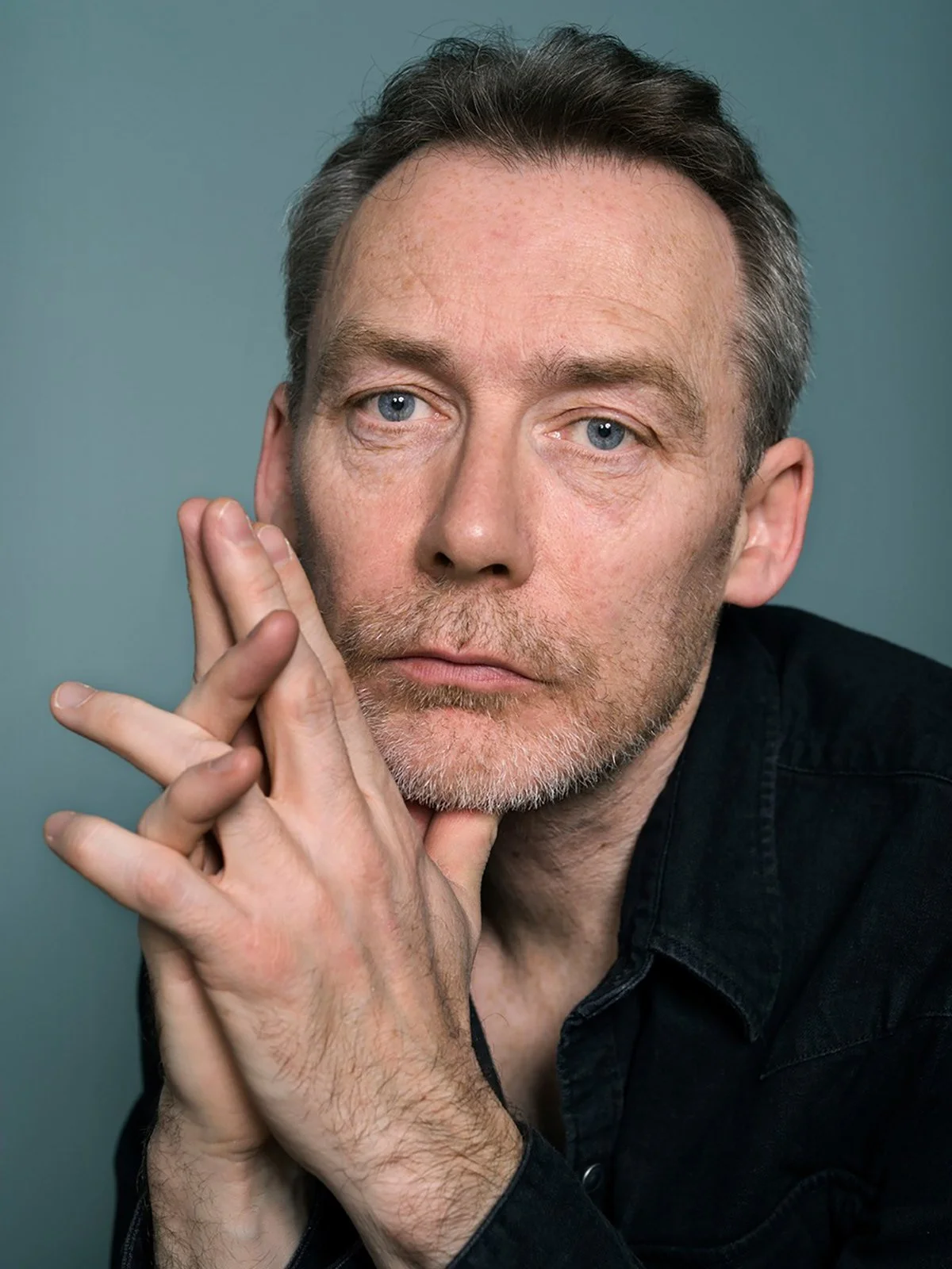 Man with clasped hands wearing a dark shirt against a teal background