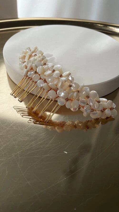 Pearl and gold hair comb with decorative pearls on a metallic surface