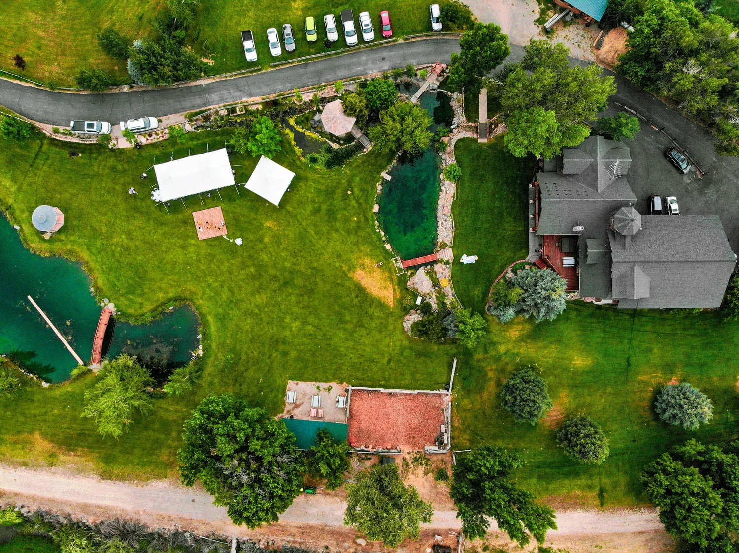 Top-down drone view of an outdoor event venue with ponds, white tents and parking