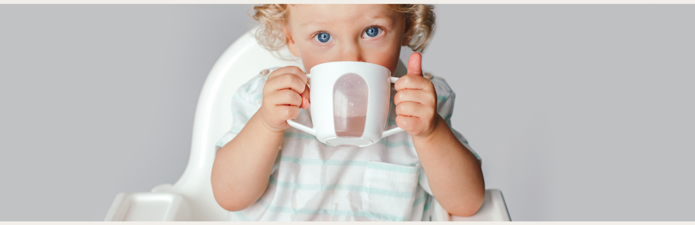 baby sitting in high chair drinking from a cup with both hands