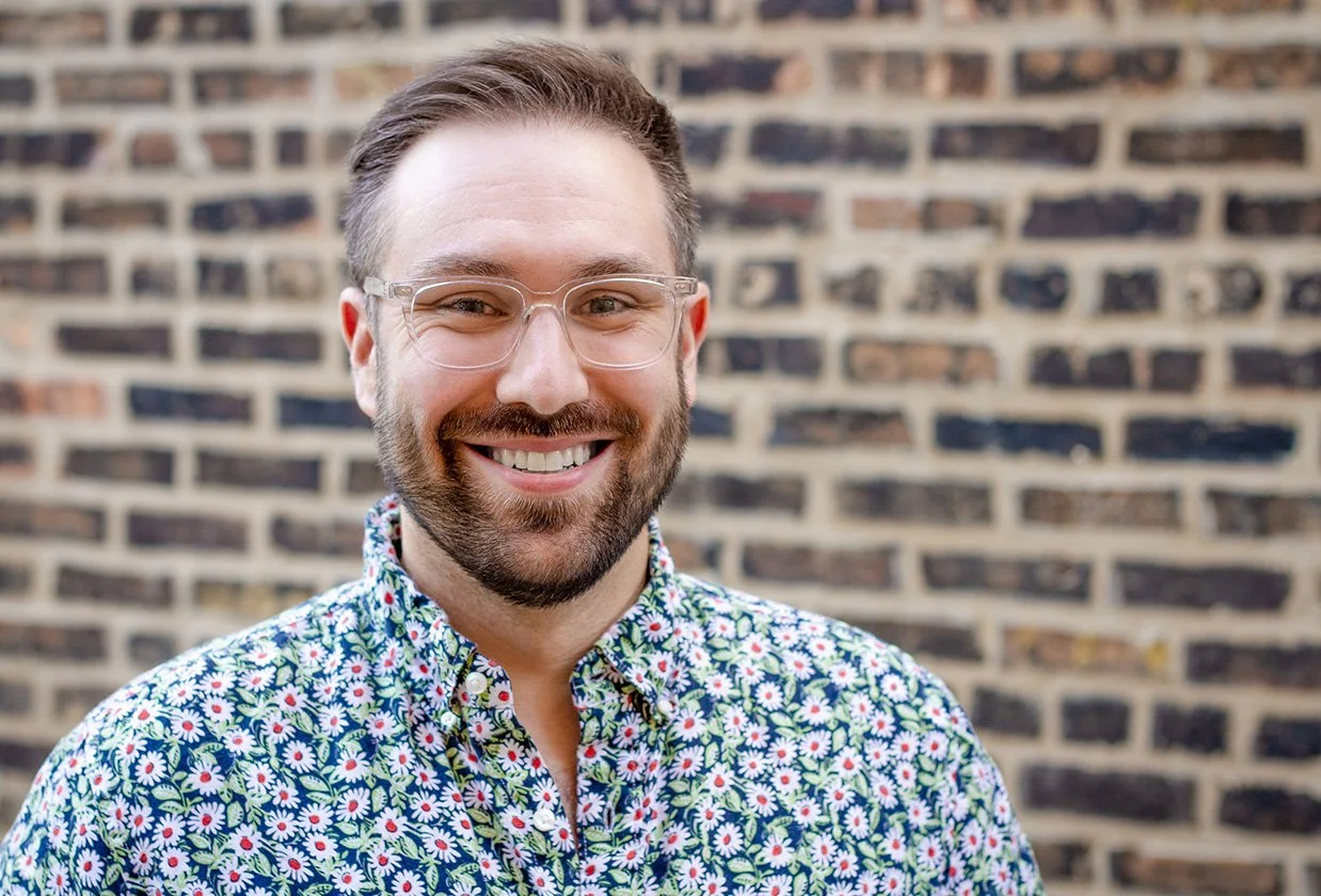 Editor and Producer Jon Gollner with glasses and a floral shirt standing in front of a brick wall.