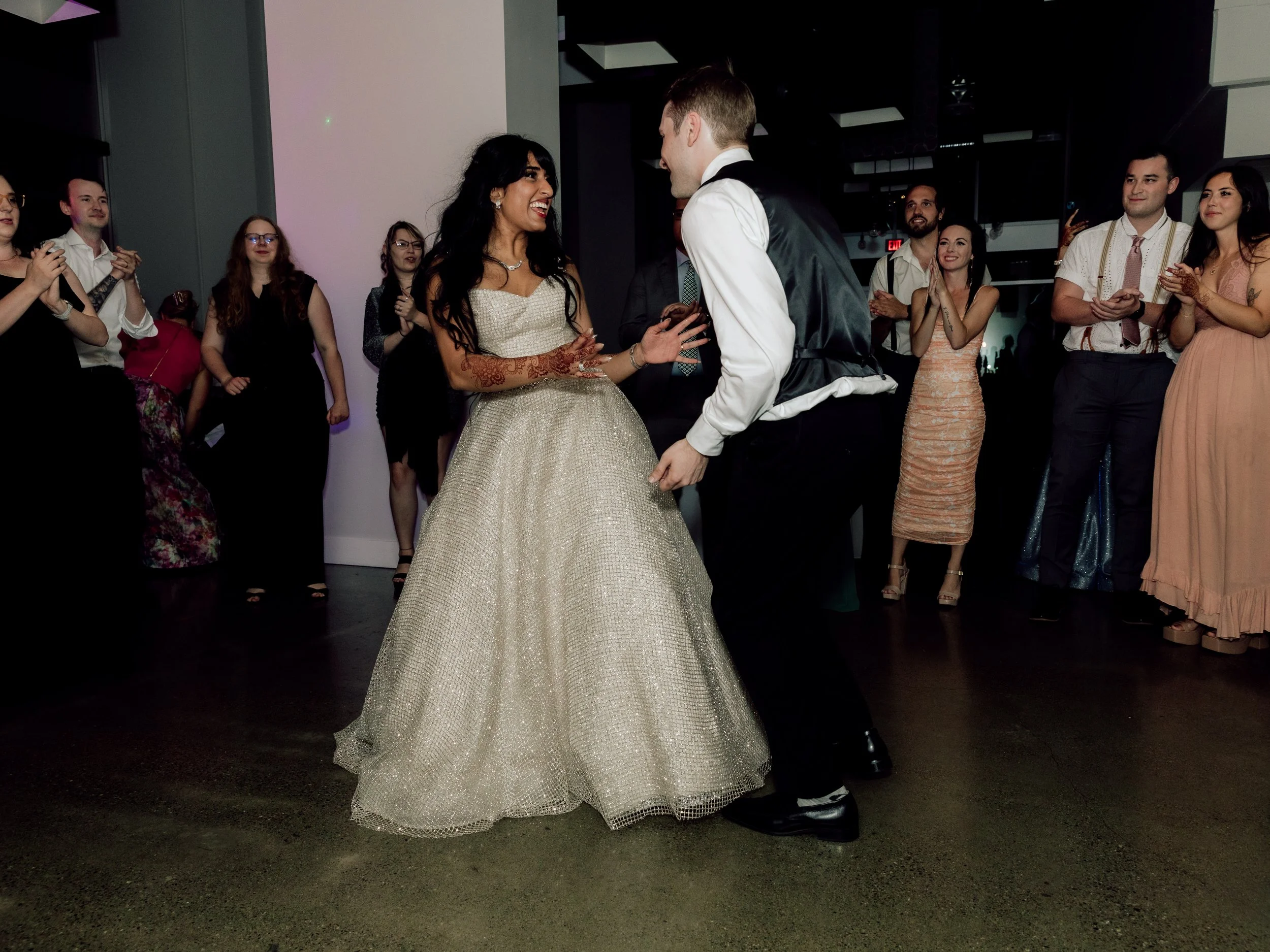 A bride and groom dancing at their wedding reception, surrounded by friends and family, on a darkened dance floor.