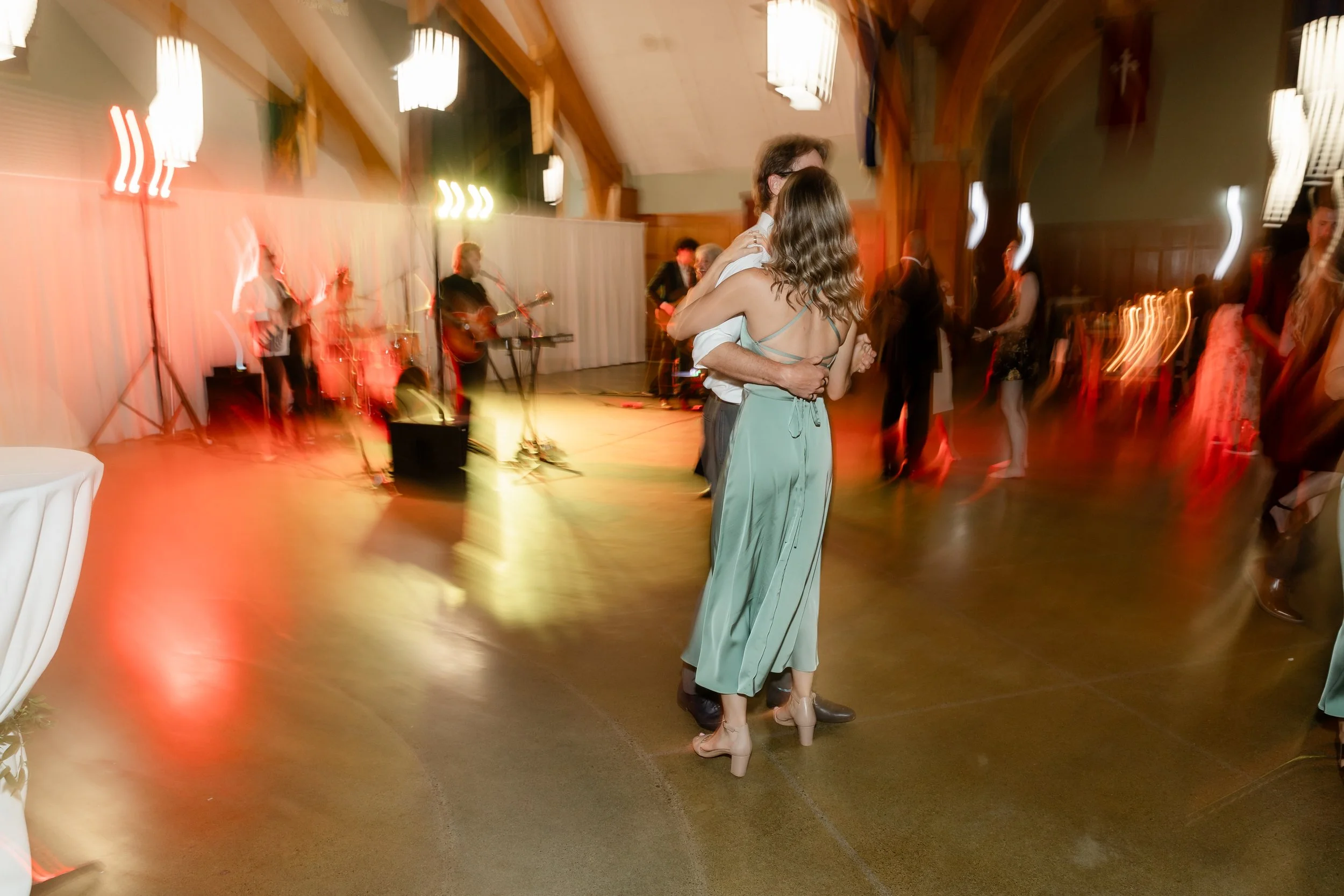 Couple dancing closely at a wedding reception with a band playing on stage in the background, blurred motion effect on the dance floor.