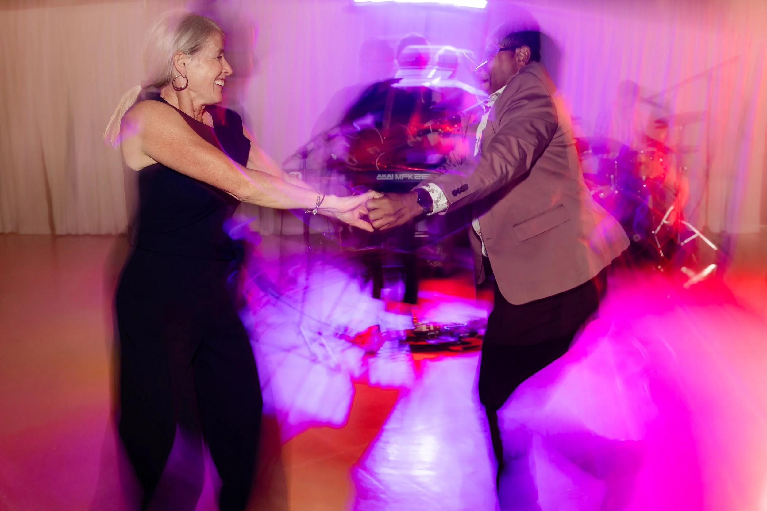 A woman and a man dancing together at a party with colorful lights, holding hands and smiling.