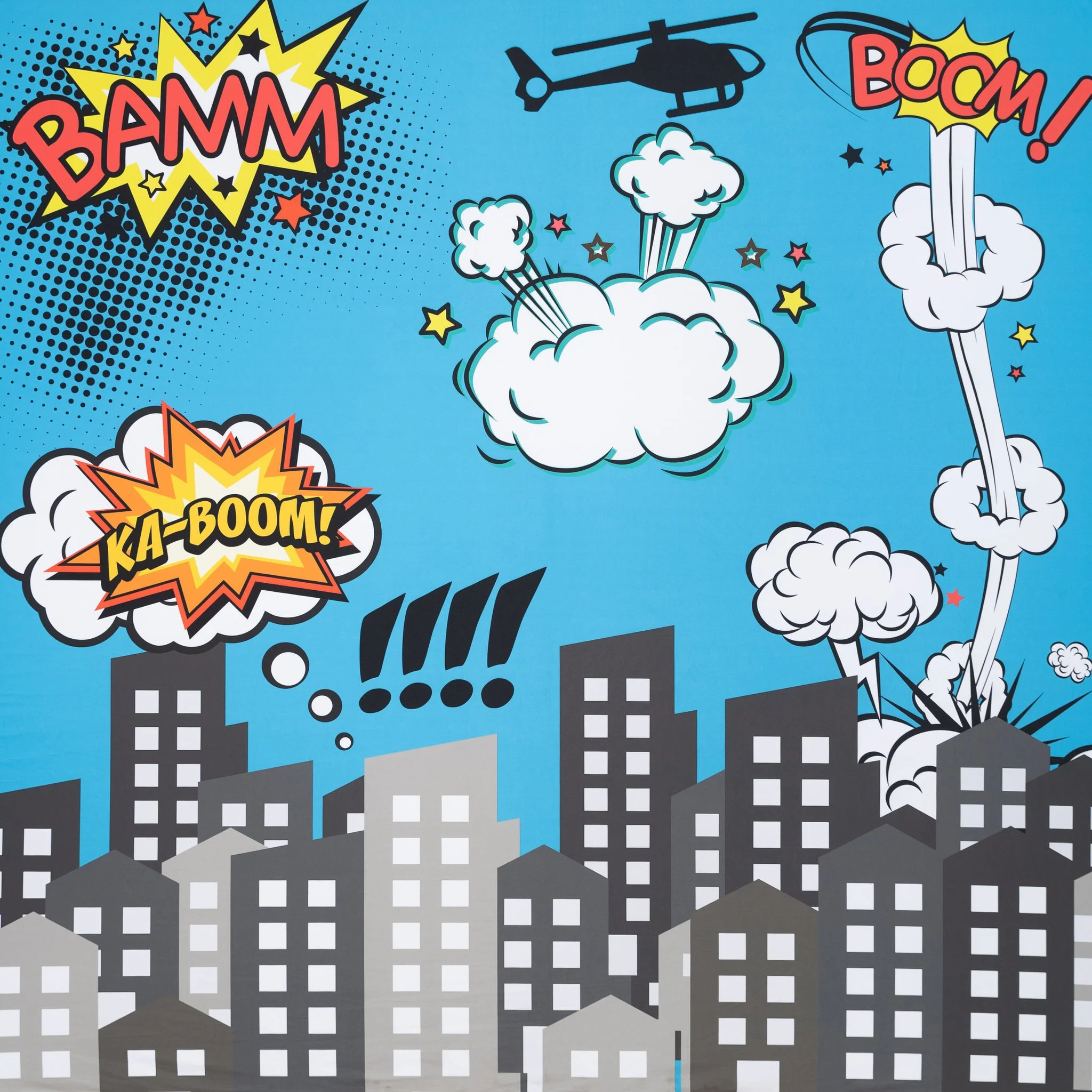 Comic-book style illustration of a city under attack with explosions, clouds, and a helicopter in the sky. Action words like 'BAM!', 'BOOM!', and 'KA-BOOM!' are displayed in colorful speech bubbles.