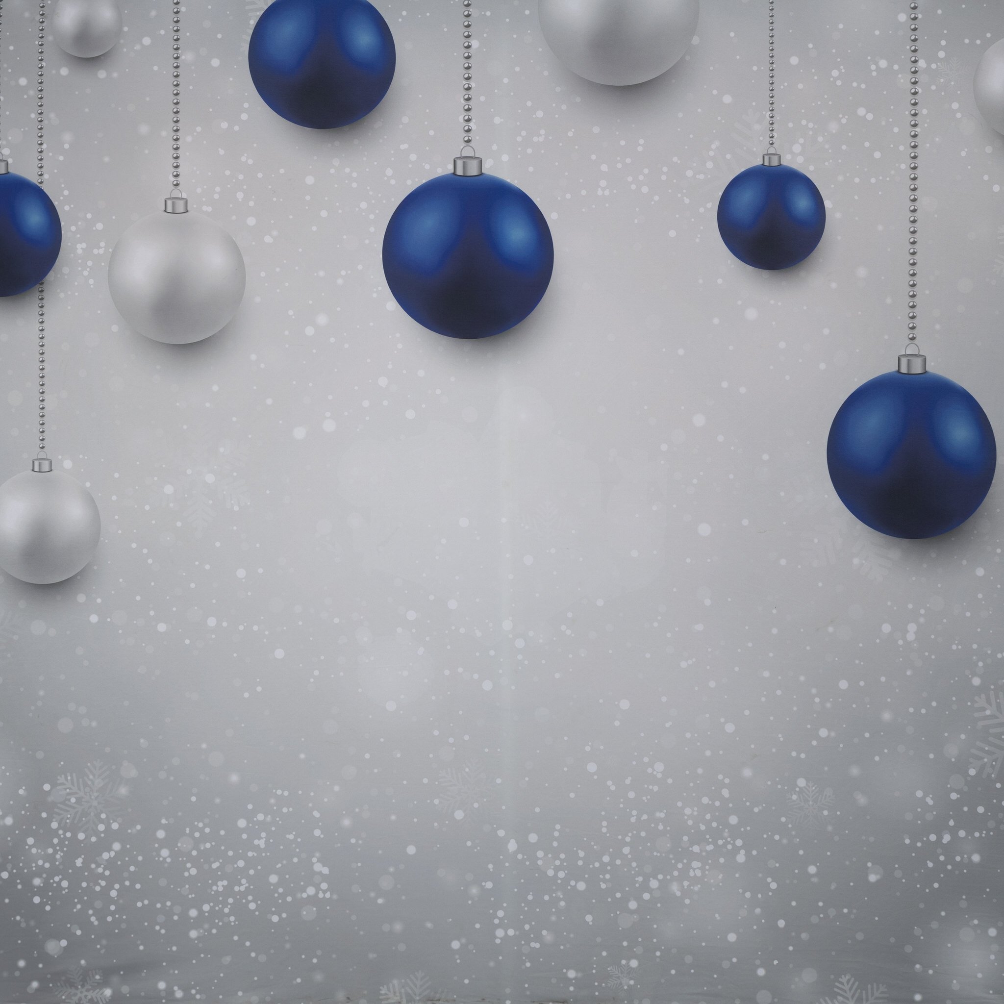 Blue and silver Christmas ornaments hanging against a snowy background.
