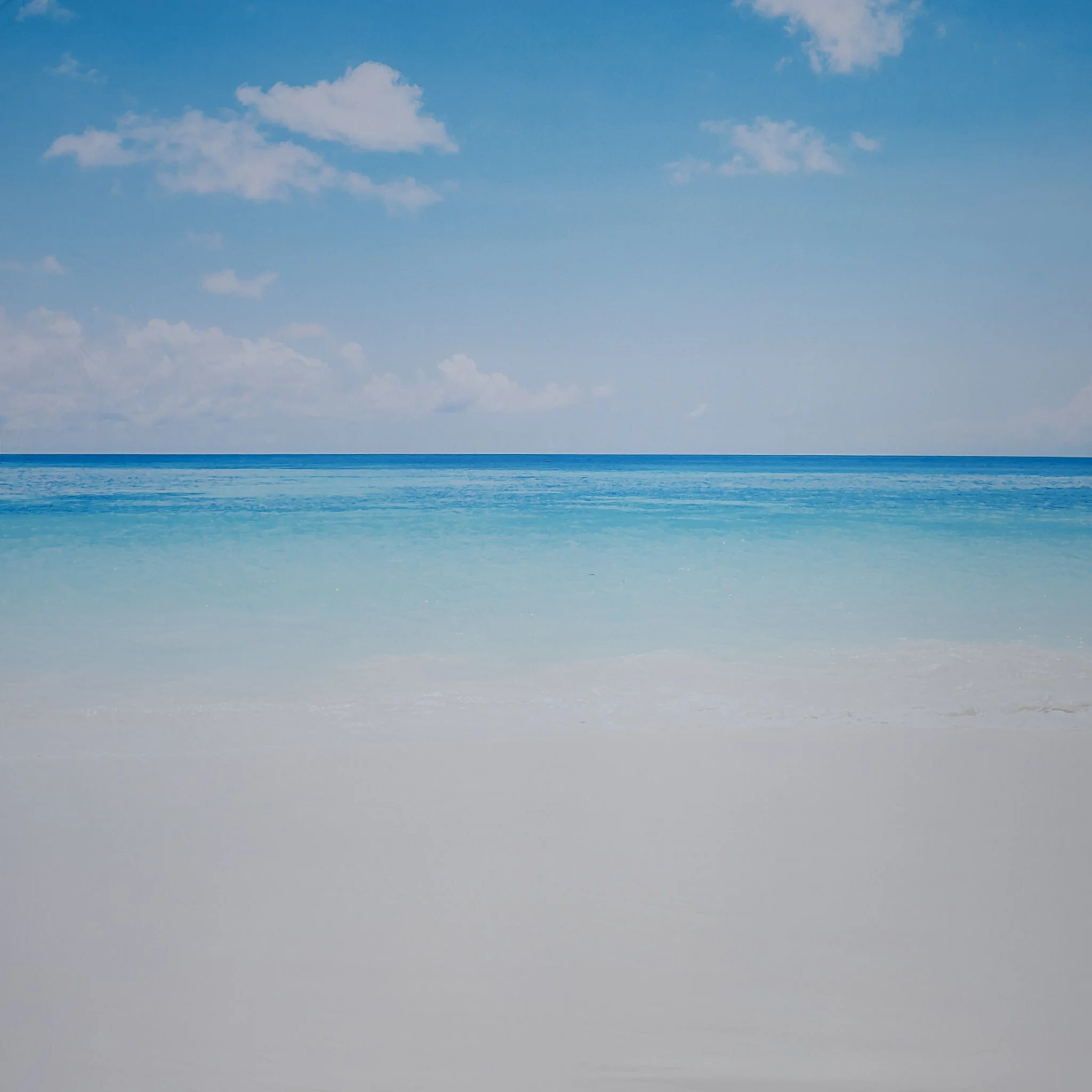 Calm ocean with gentle waves, blue sky with scattered clouds, white sandy beach