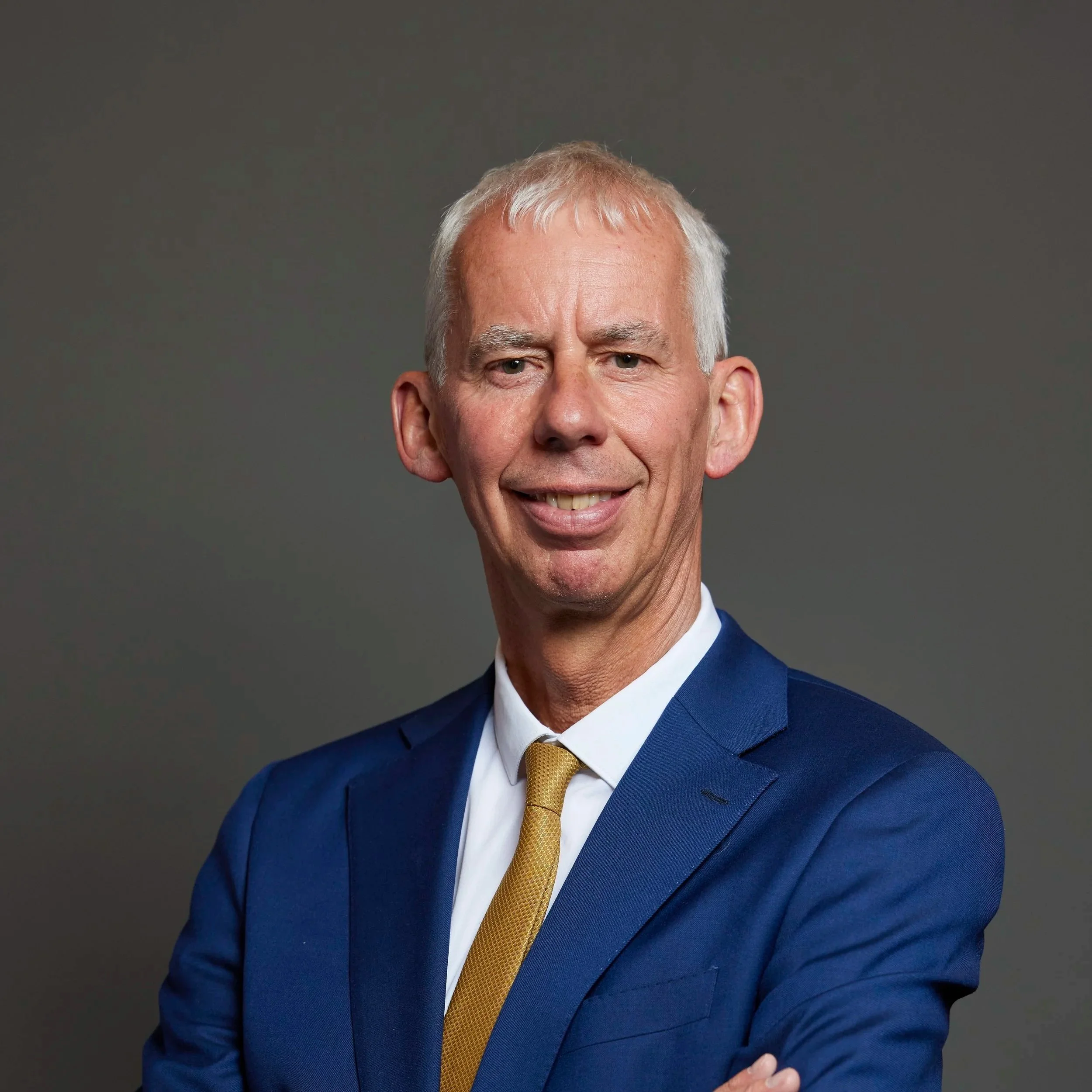 Official Portrait of John Milne MP. A man with short white hair in a blue suit.