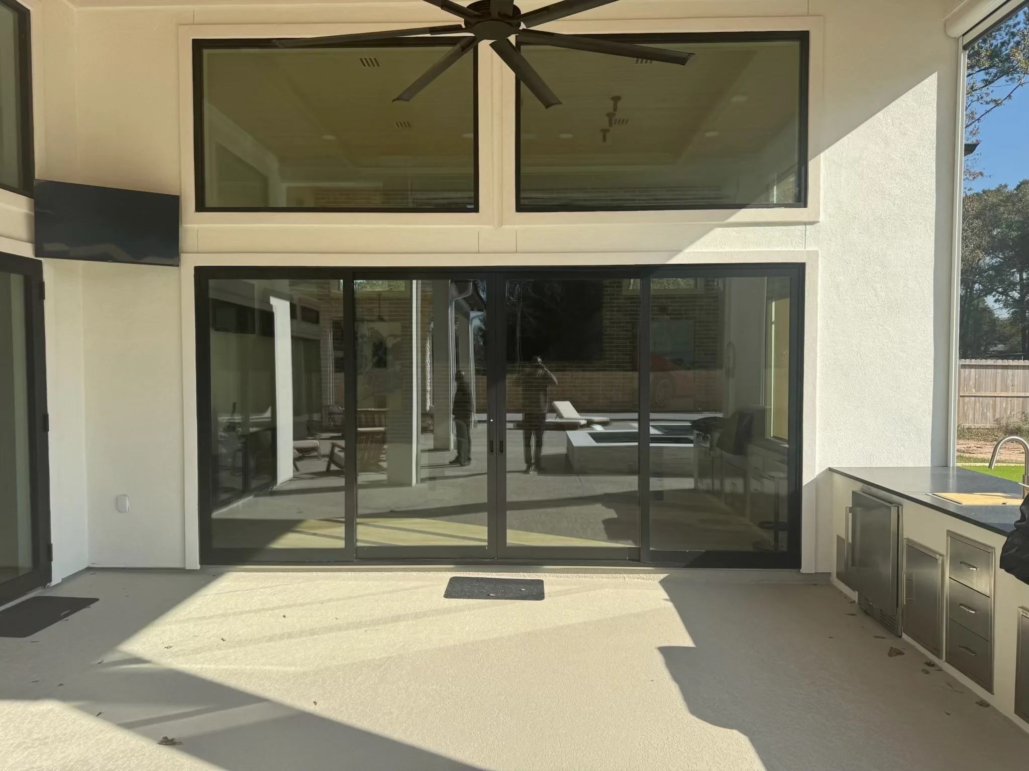 A backyard patio area with sliding glass doors, a ceiling fan, and outdoor kitchen appliances visible on the right.