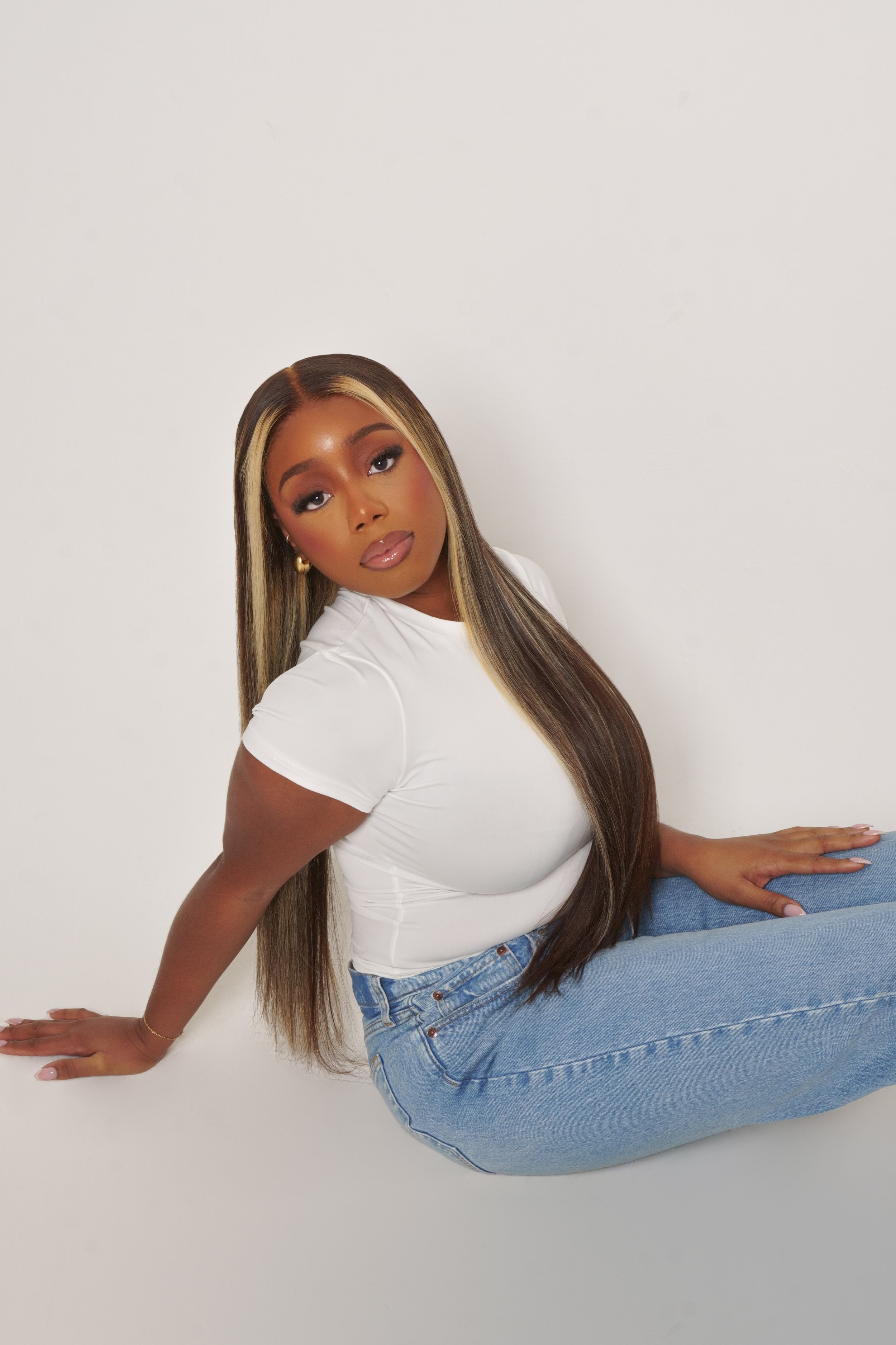 Model sitting on the floor with highlighted hair wearing white t-shirt and blue jeans