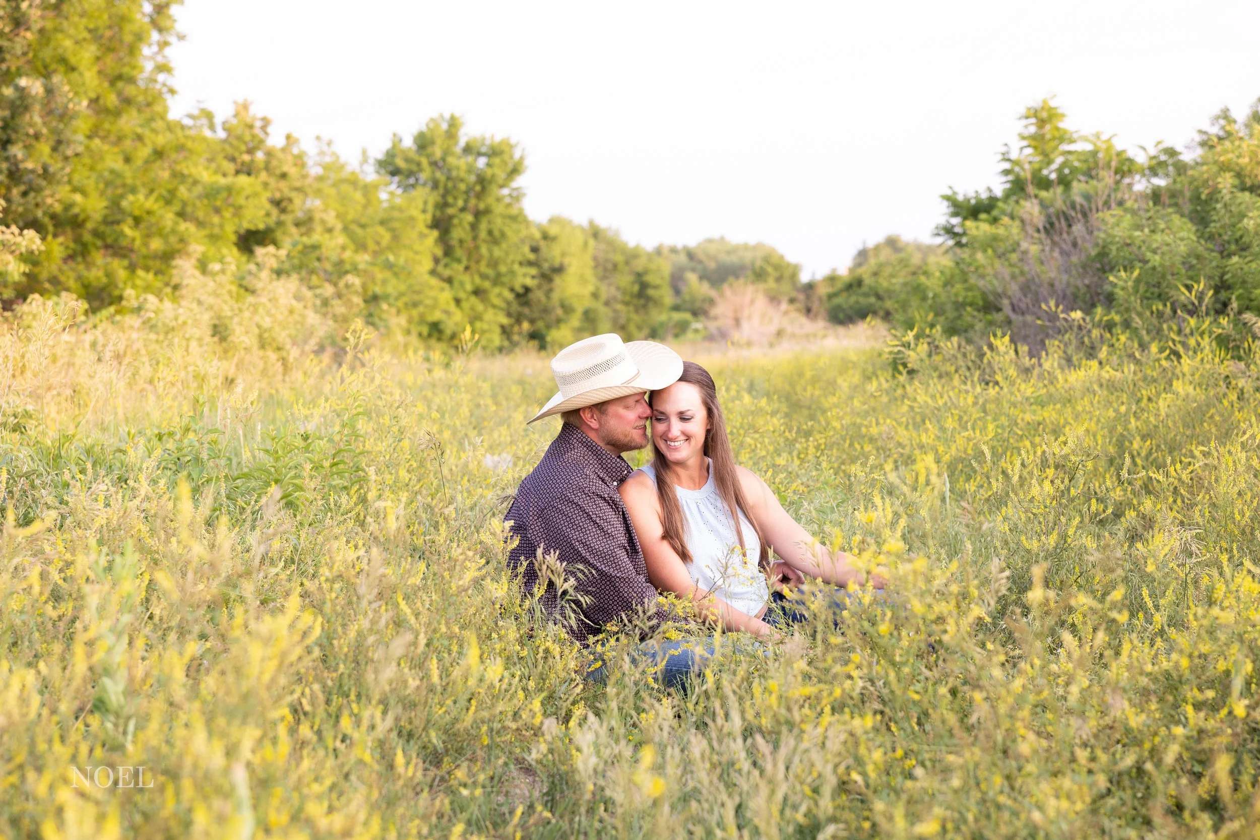 Engaged couple sitting in a field of yellow flowers