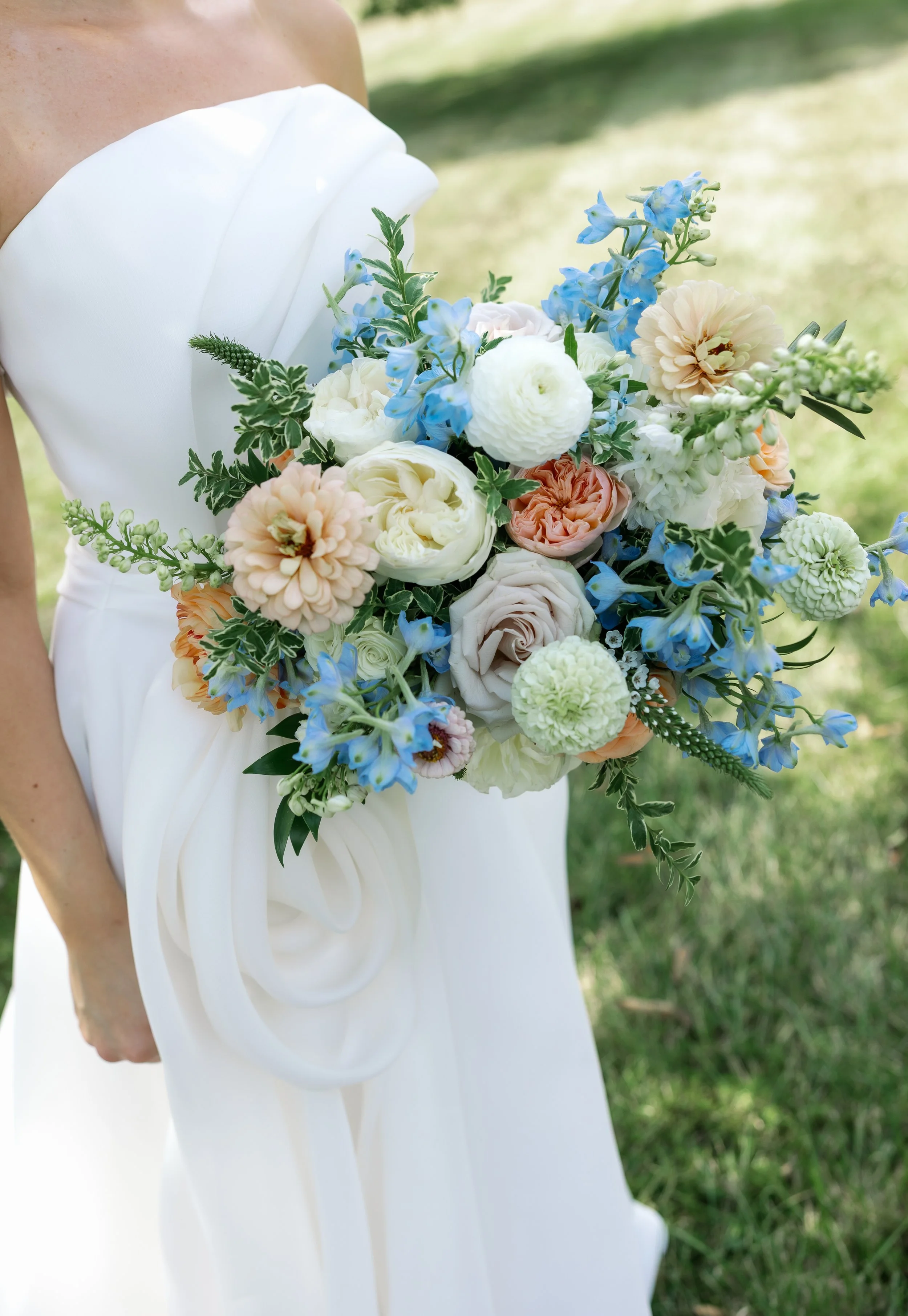 A detailed close-up of Callie’s pastel blue bridal bouquet featuring white blooms and soft peach accents. The delicate summer florals highlight her romantic, airy wedding style—perfect inspiration for brides searching for pastel color palettes and ti