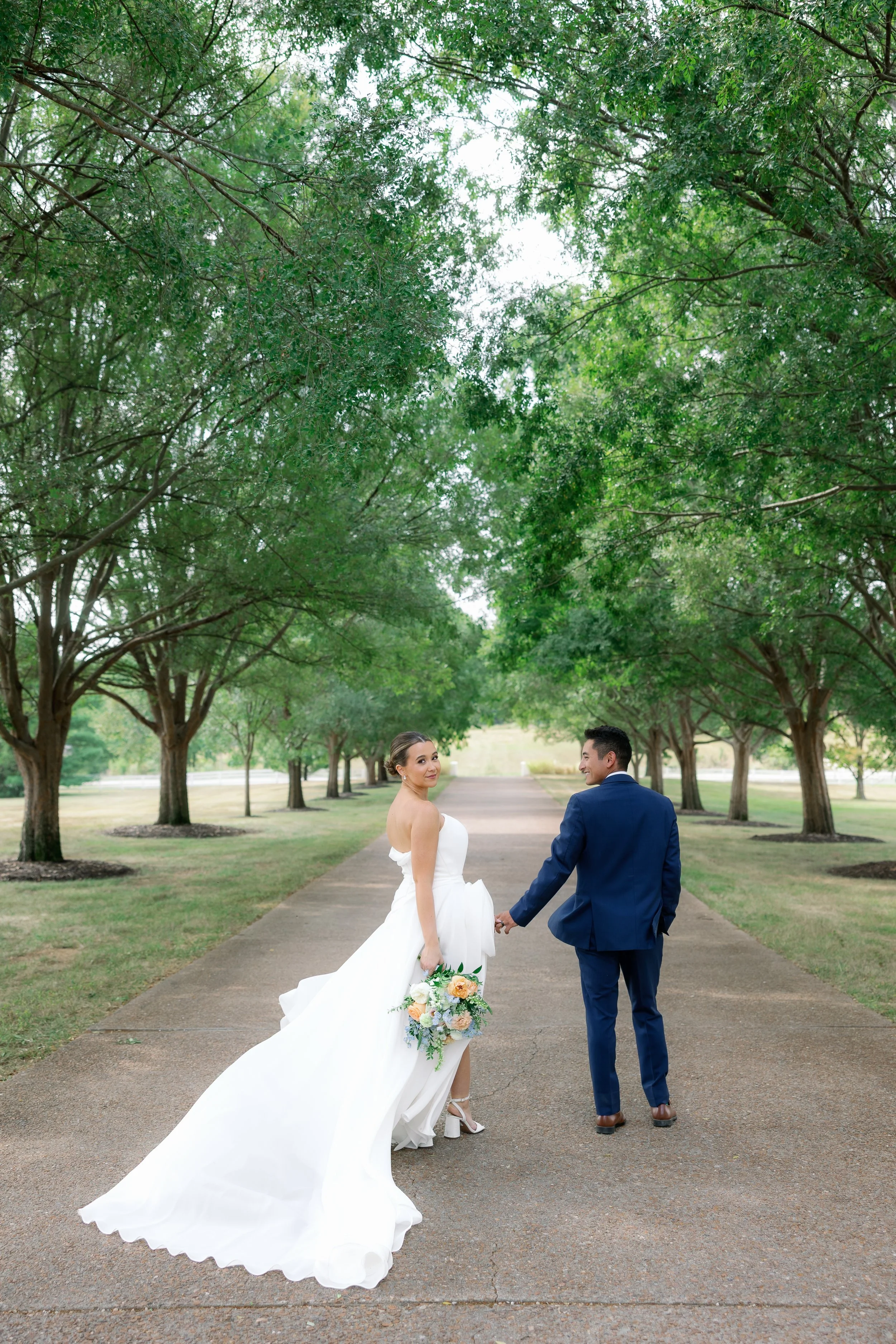Callie and Austin walking down the driveway at the Callaway Jewel in Fulton, Missouri with soft blue and peach wedding florals enhancing the scene.