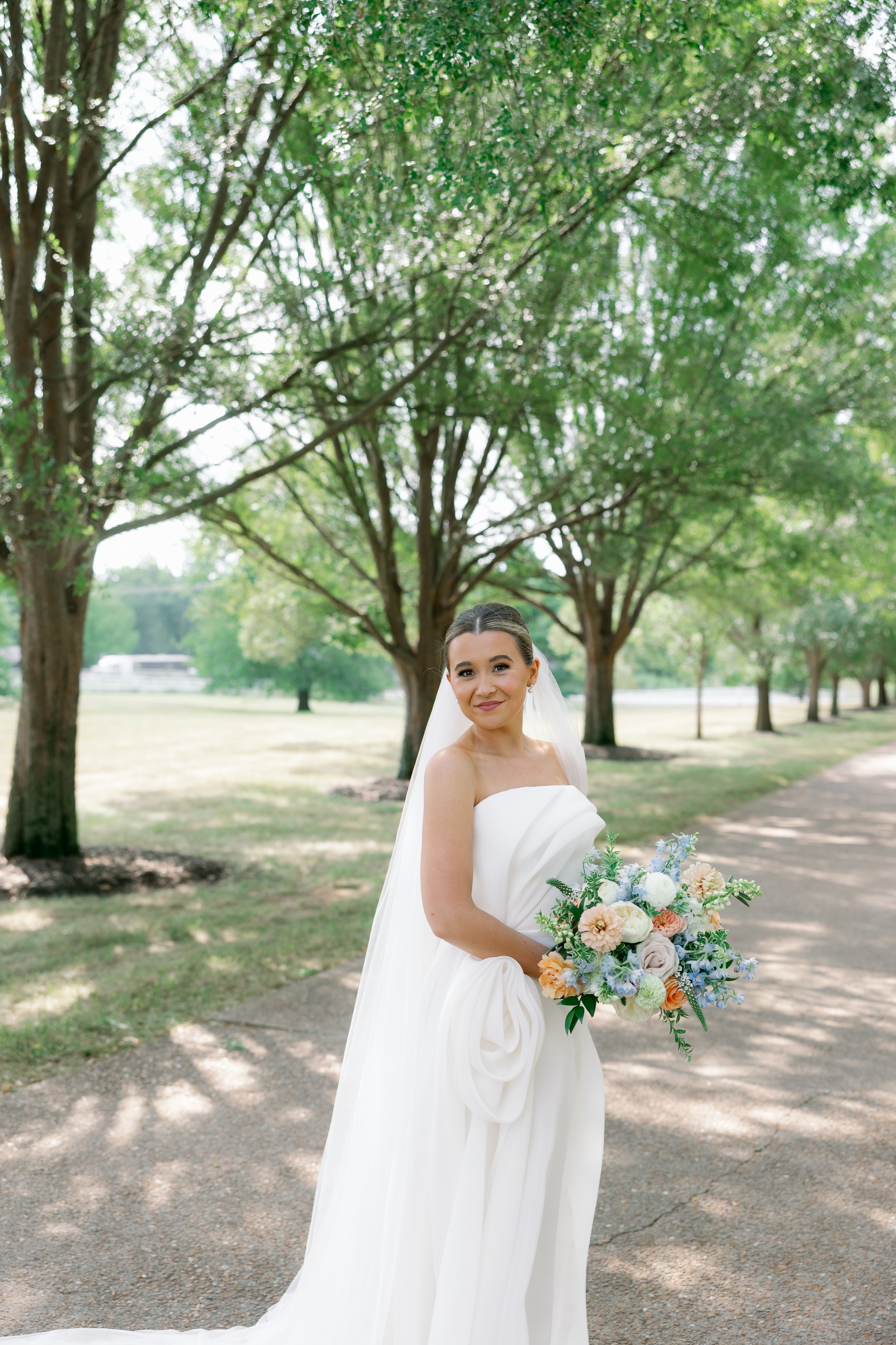 A floral-focused image showing Callie’s bouquet held at her waist, highlighting the contrast between the pastel flowers and her classic wedding gown. Perfect SEO for brides searching "blue bridal bouquet with peach accents."