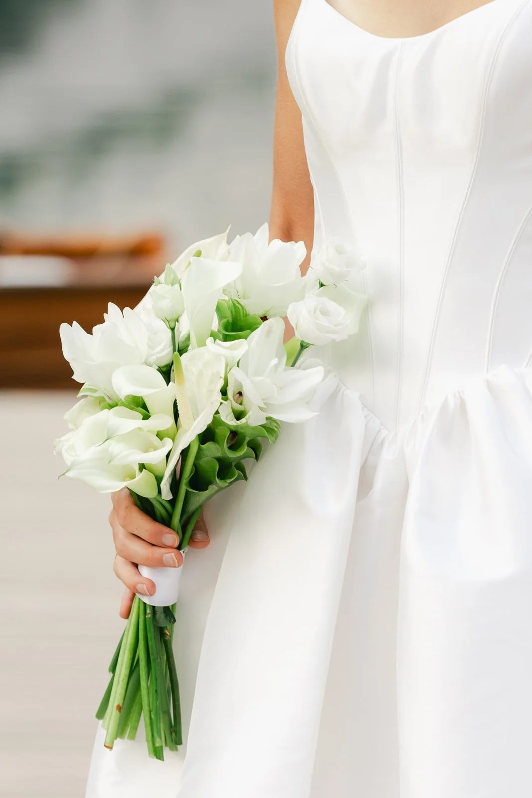 A bride holding a bouquet of white calla lilies and roses, wearing a white wedding dress. Lago Di Braies in the Dolomites of Italy