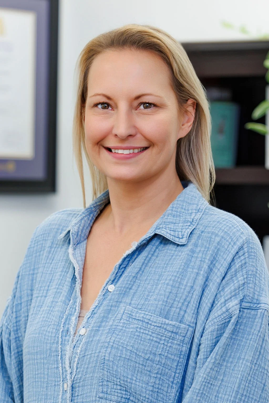 Jamie is wearing a blue denim button up shirt. She has blonde hair and is smiling.