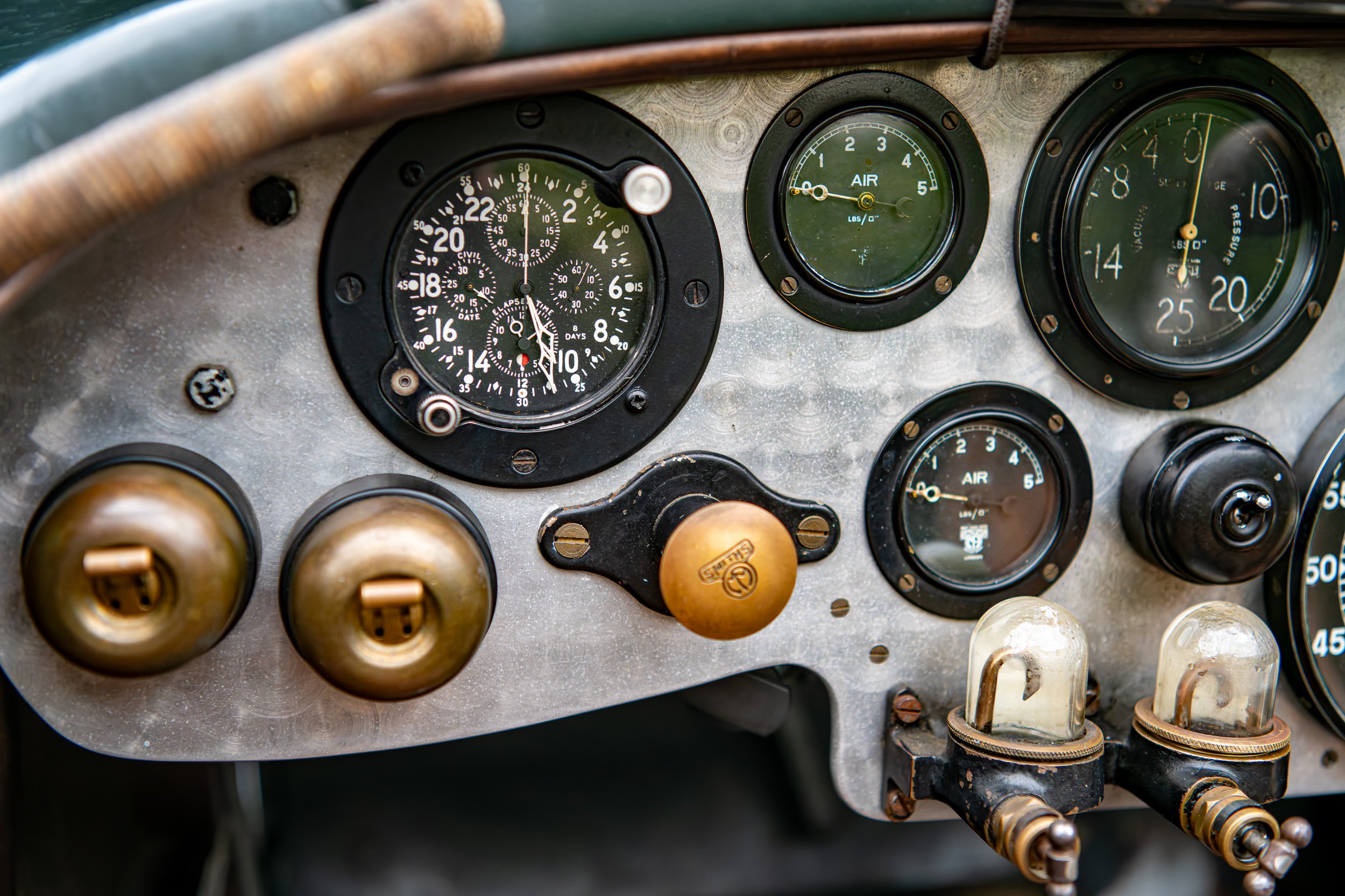 Close-up of vintage airplane cockpit instruments, including an altimeter, airspeed indicator, and various gauges, with two glass-covered electronic components in the foreground.