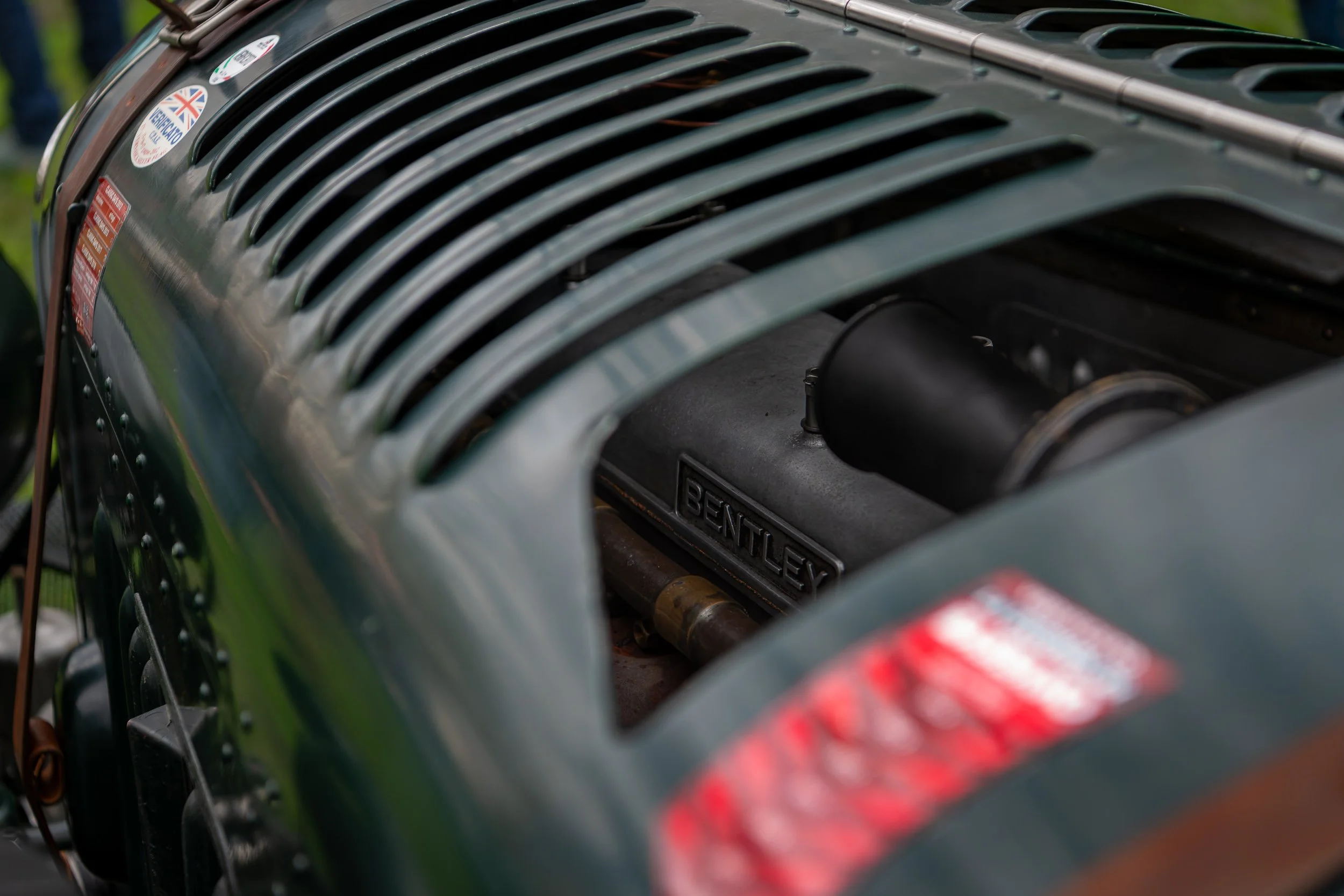 Close-up of an engine with a Bentley logo, surrounded by a dark green body with multiple vents and a few stickers.