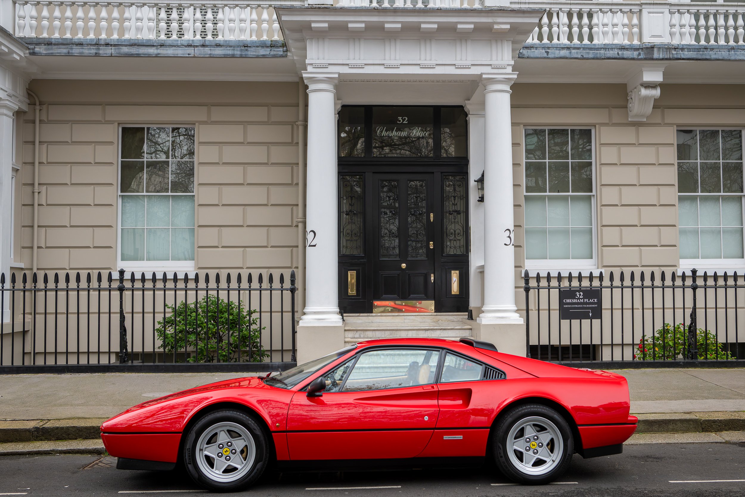Red Ferrari sports car parked in front of a beige townhouse with black door and white columns.