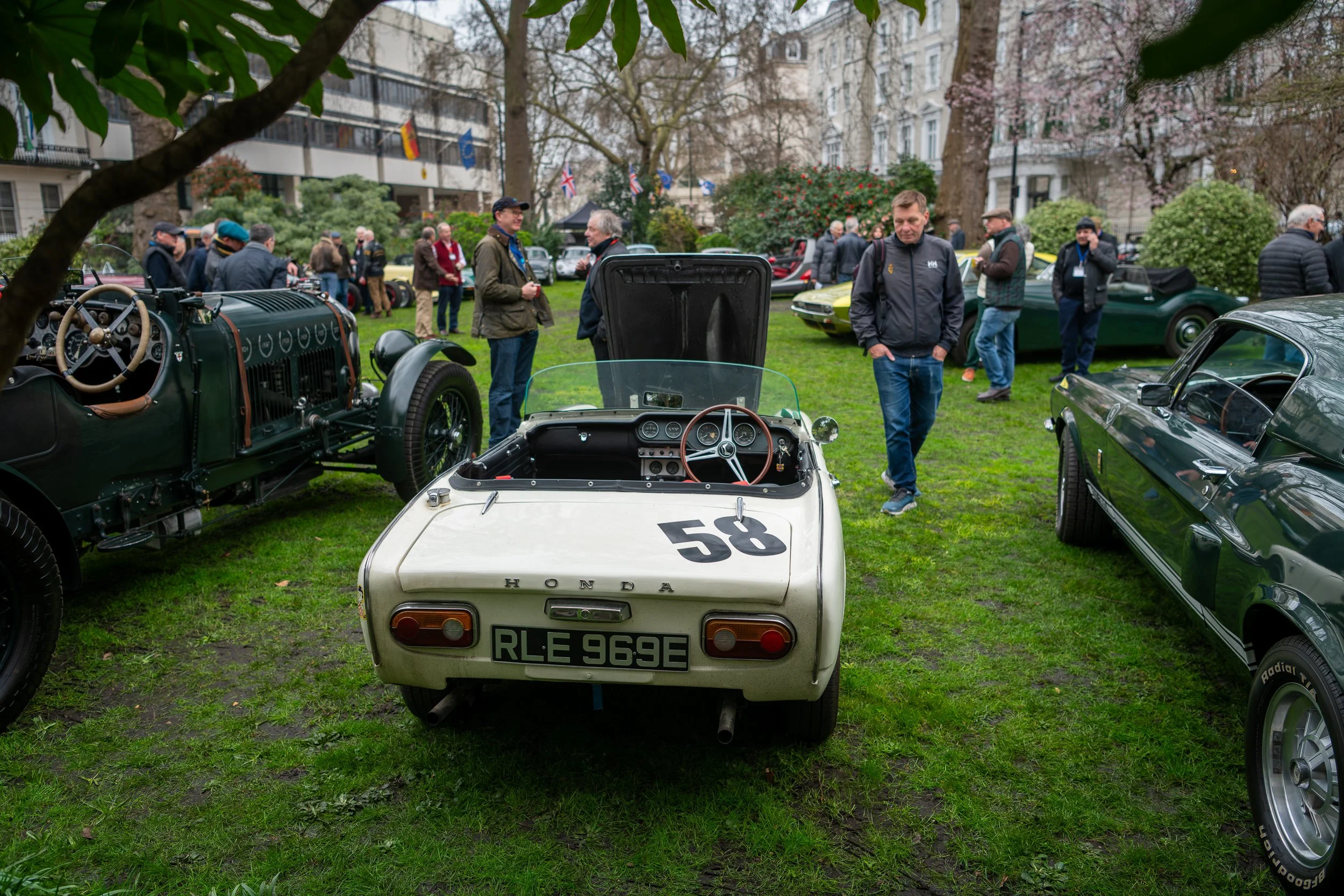 A vintage car show featuring classic and sports cars displayed on a grassy area with people walking and observing the vehicles.