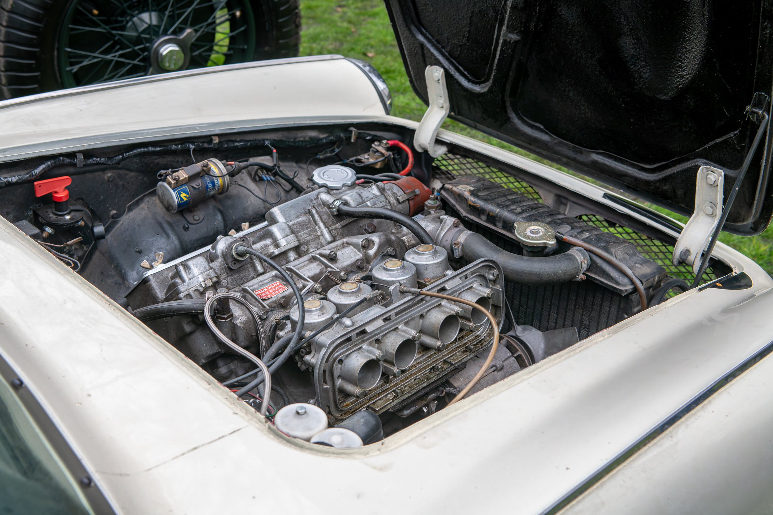 Vintage car engine with open hood, showing mechanical components and part of a black grille