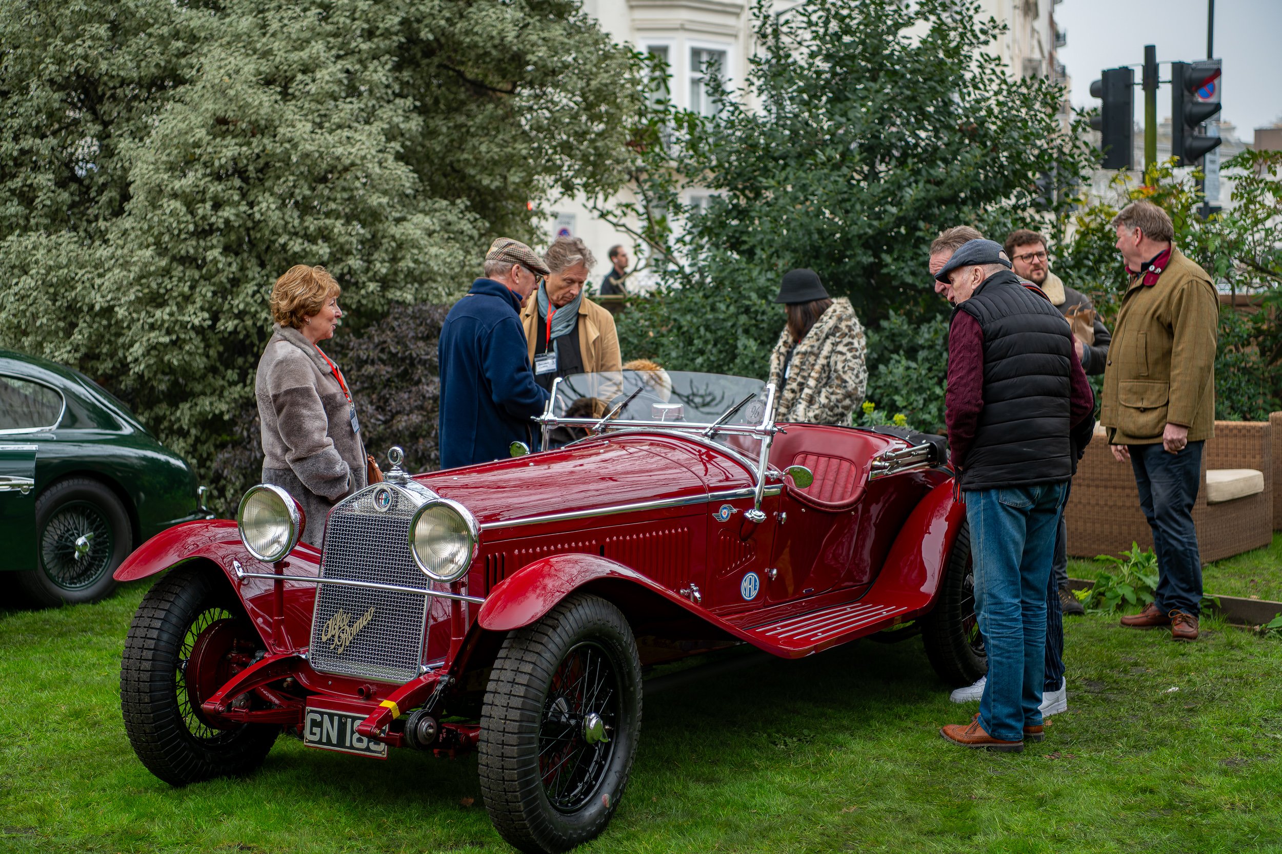 Group of people examining a vintage red convertible car at an outdoor event.