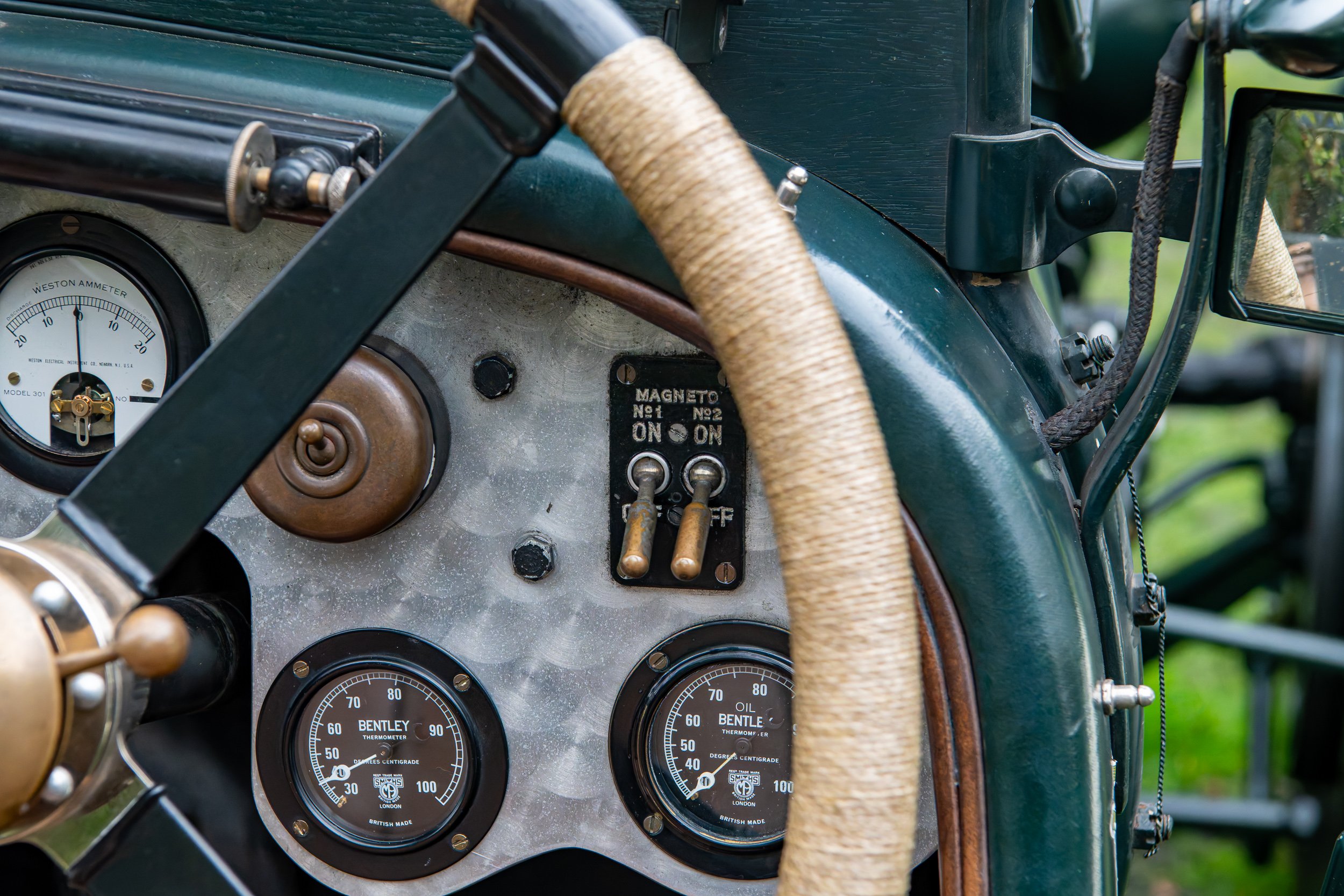 Dashboard of a vintage car with various gauges, switches, and a tightly wrapped steering wheel.