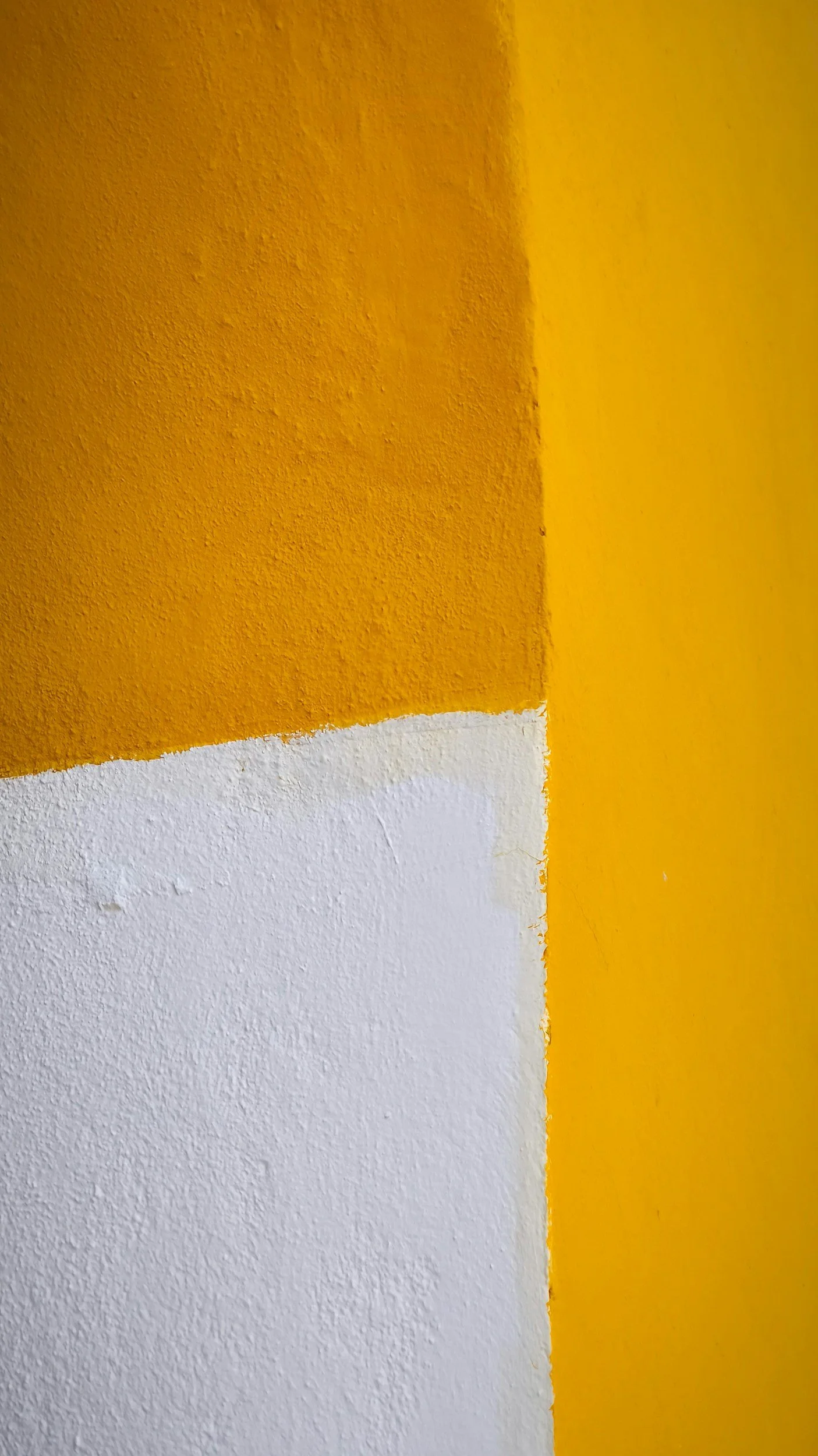 Close-up of a wall painted with yellow and white sections, showing textured drywall.