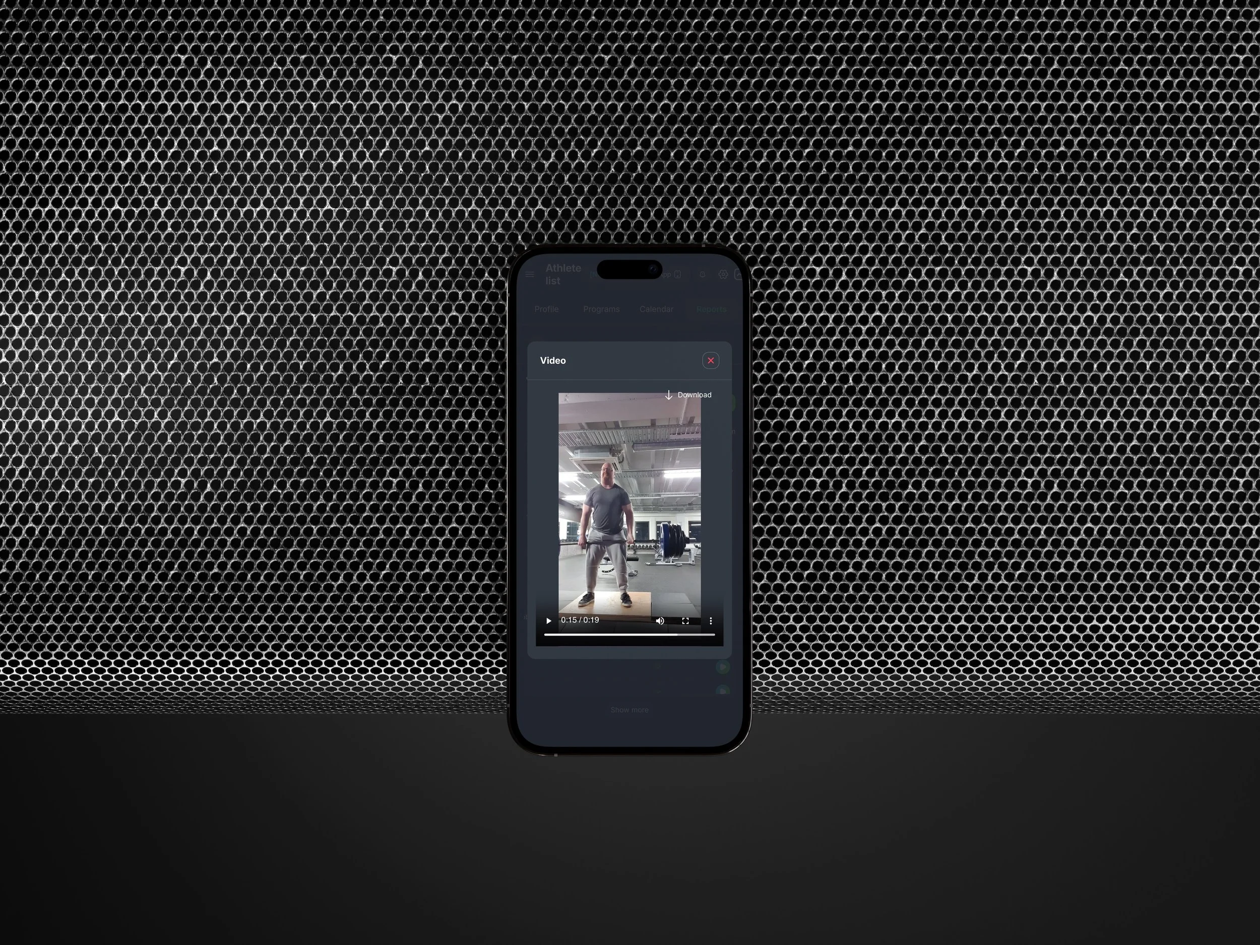 Smartphone displaying a video of a person in a gym, placed on a black surface with a textured gray background.