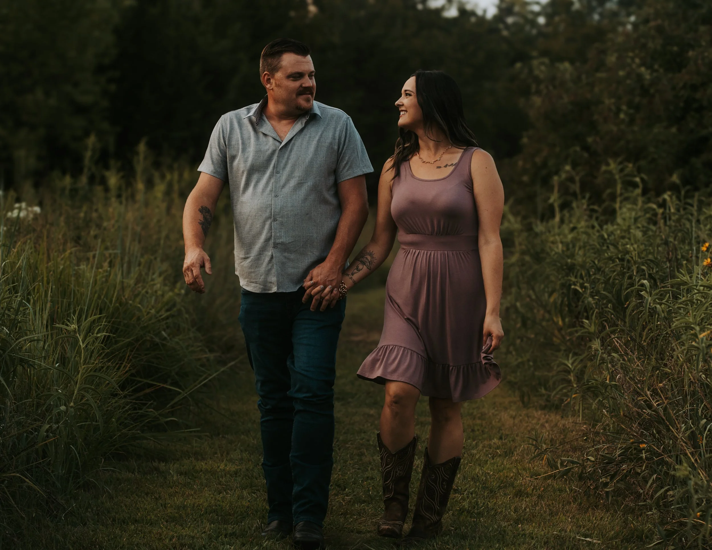 Wichita couple walking hand in hand outdoors, woman smiling at husband, captured in a moody, candid, and timeless photography session by affordable local photographer