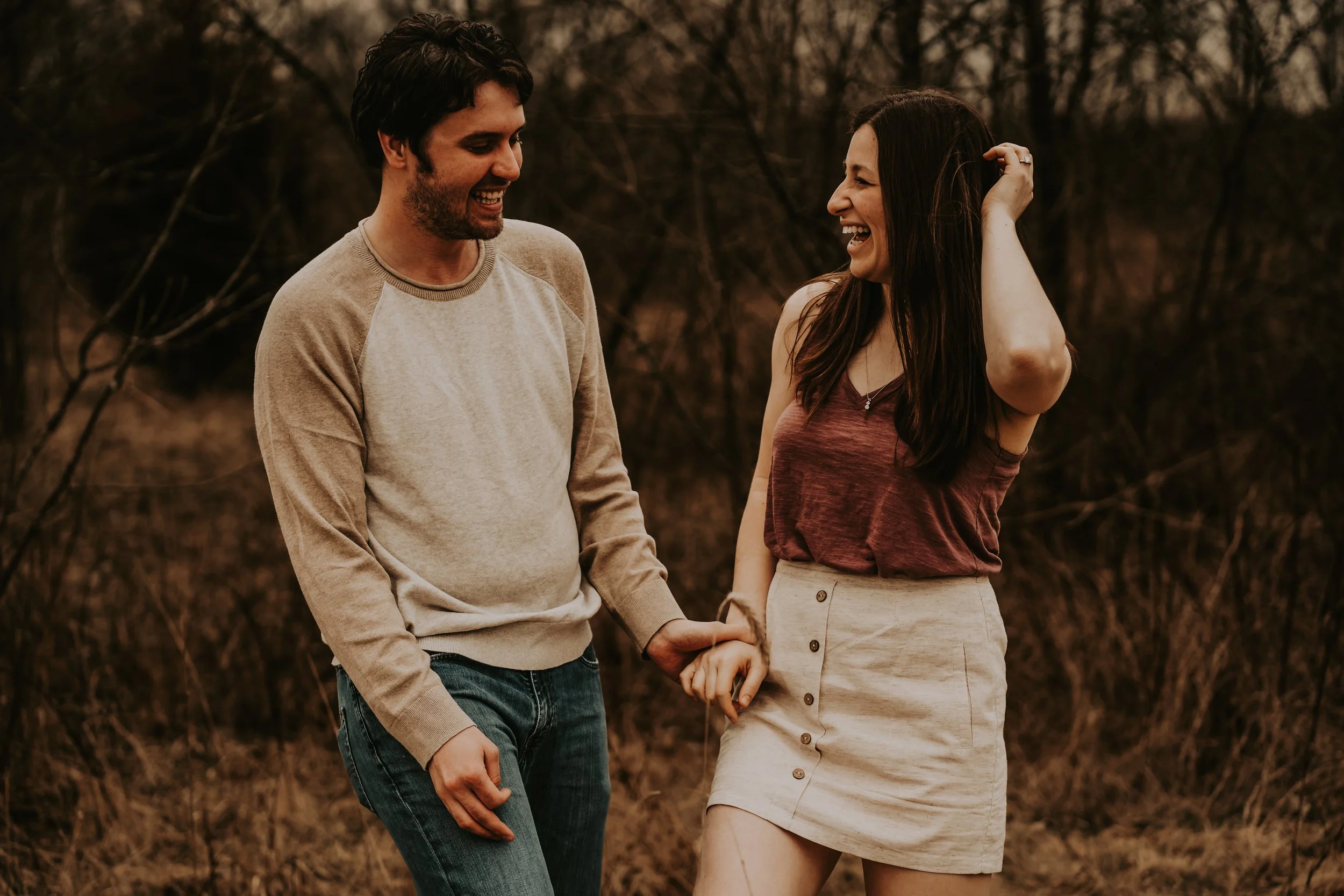 Engaged couple in Wichita holding hands and giggling outdoors, captured in a moody, candid, and romantic photography session by an affordable local photographer