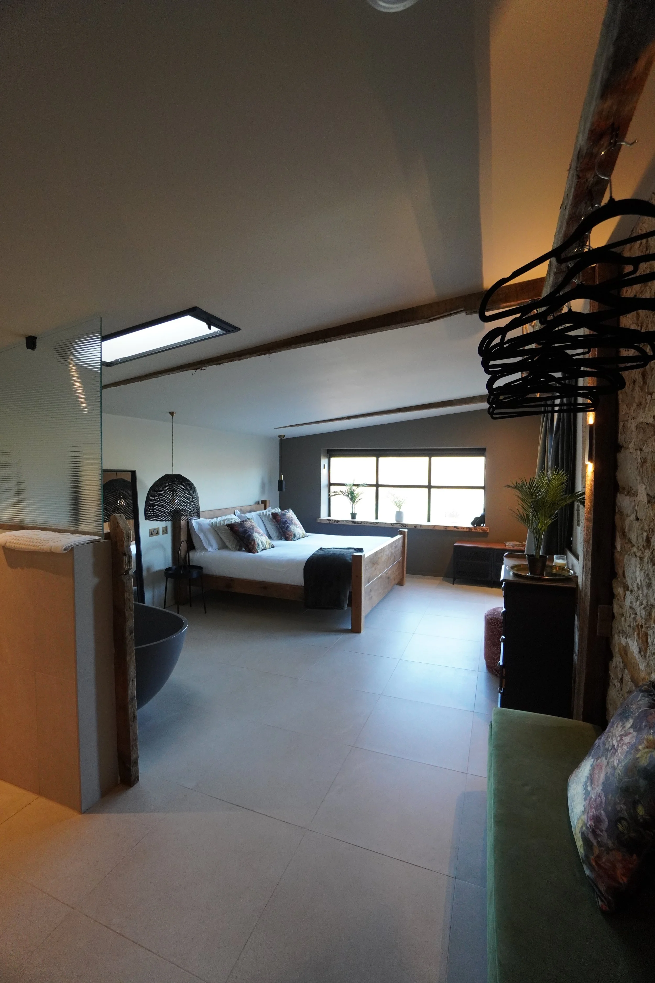 Interior of a modern bedroom with a large bed, black pendant lights, a green couch, and a window with plants on the sill.