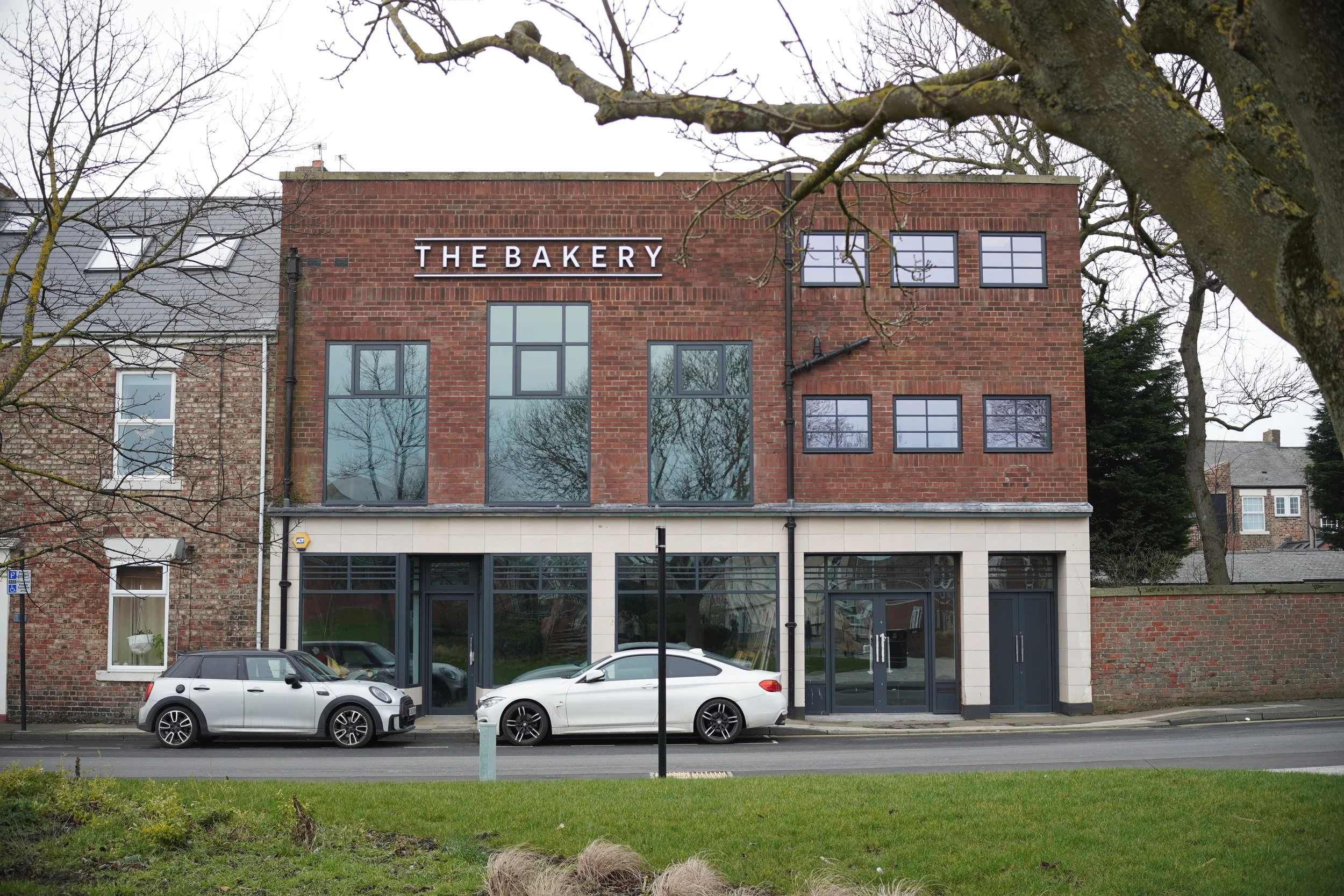 PWS Architecture + Design Ltd — A three-story brick building with a sign that reads 'THE BAKERY' on the upper front, featuring large windows on the ground and middle floors, and smal