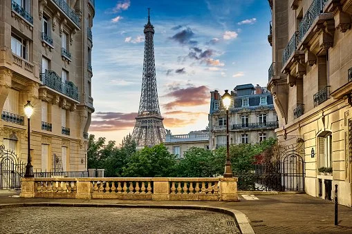 View of the Eiffel Tower seen from a Paris street with classic Parisian buildings and street lamps, during sunset.