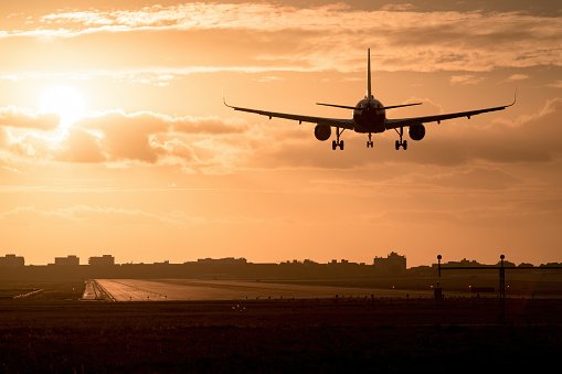 An airplane approaching for landing during sunset with a cloudy sky and runway visible below.