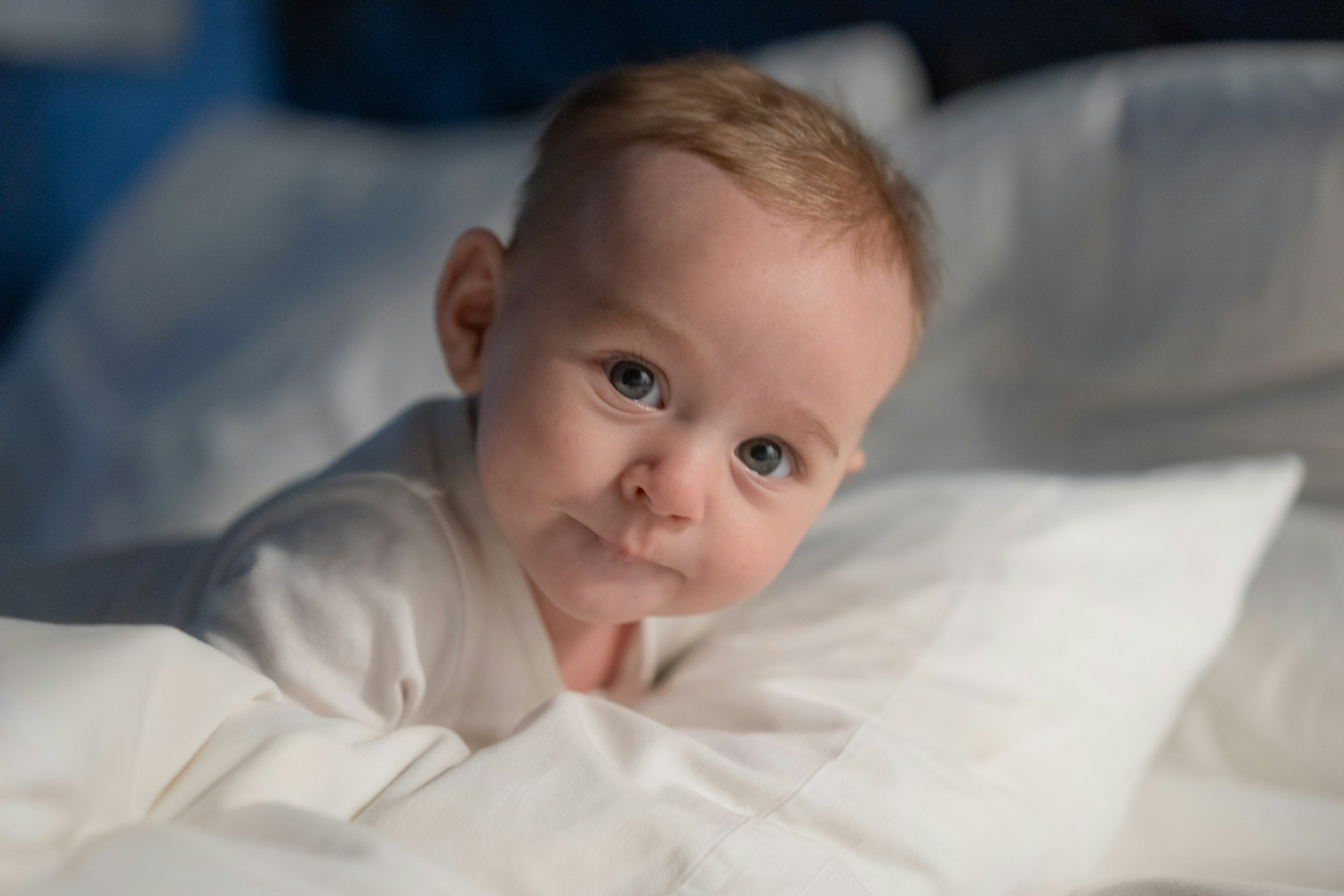 Close-up of a young child with red hair and blue eyes lying on a bed, looking directly at the camera.