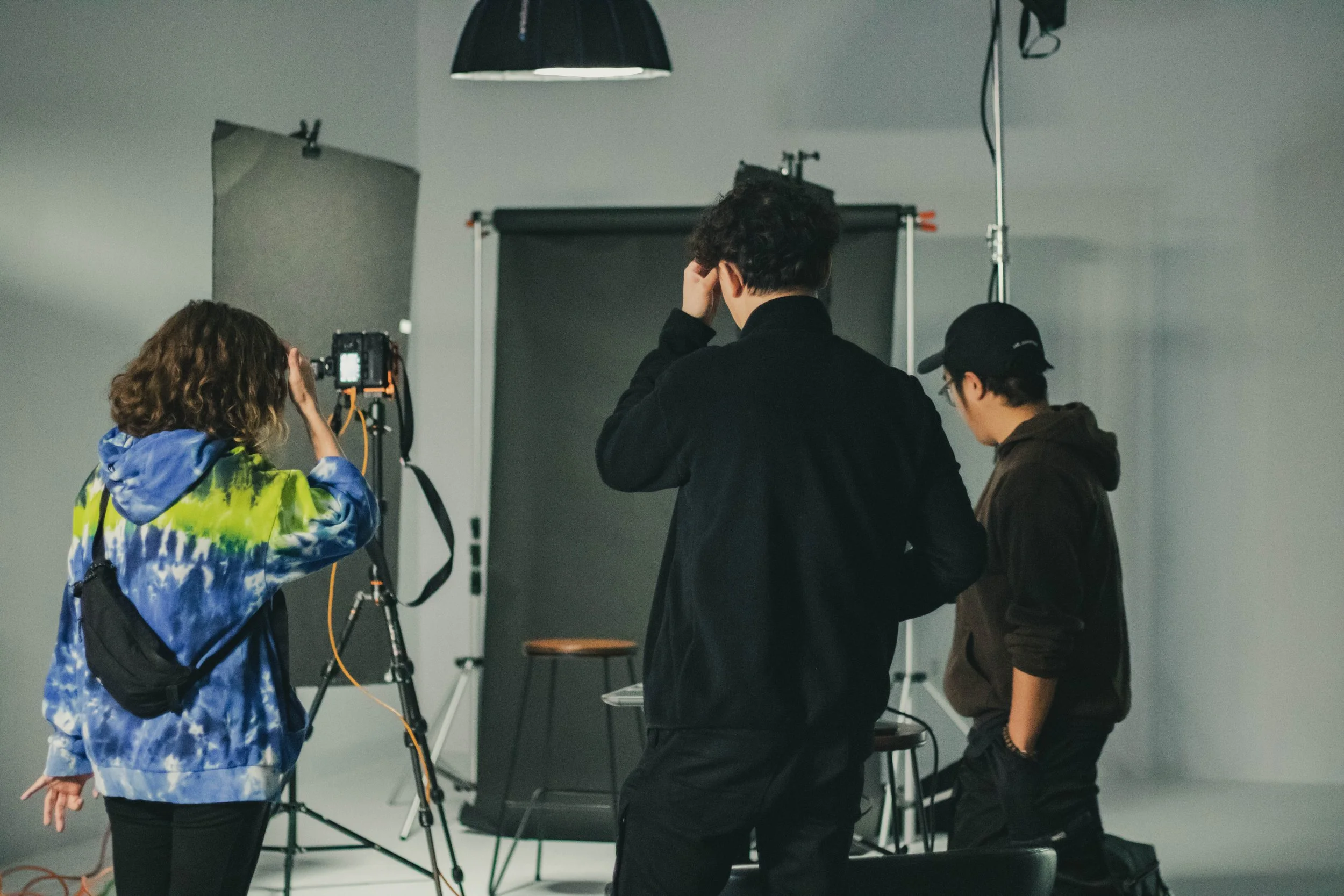 Trois personnes dans un studio de photographie ou tournage, avec un fond gris, un support et un éclairage