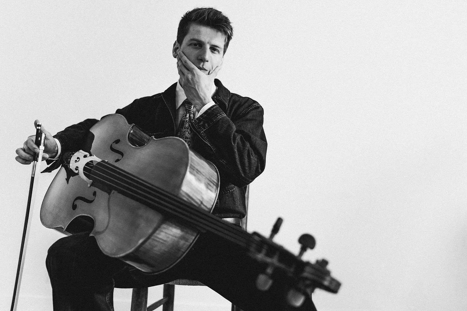 Homme jouant de la guitare acoustique noir et blanc, assis avec un micro, main sur le visage, regard pensif, fond blanc.