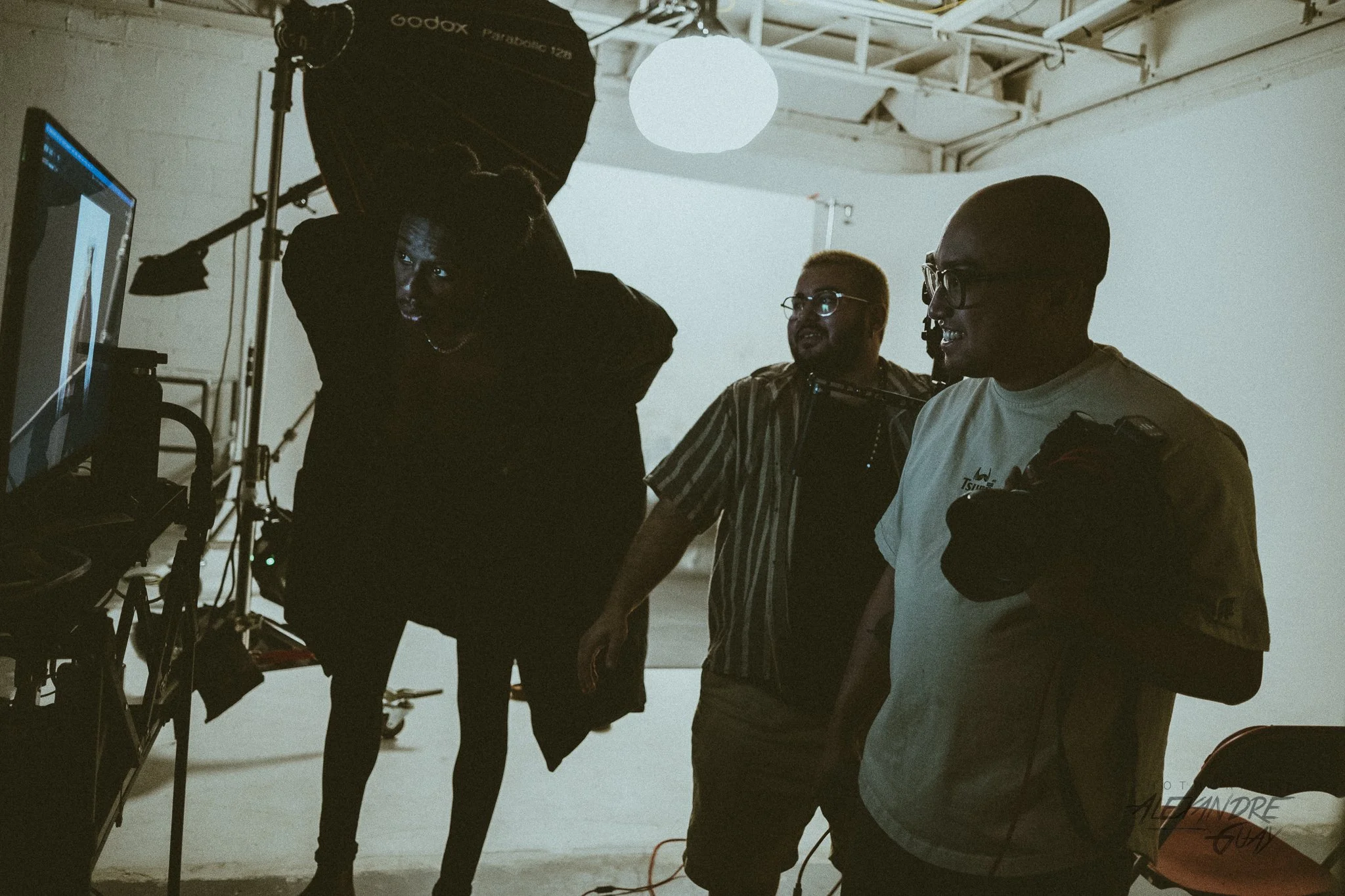 A photographic production team in a studio, with a white background, using studio lighting and a computer monitor, with members in conversation.