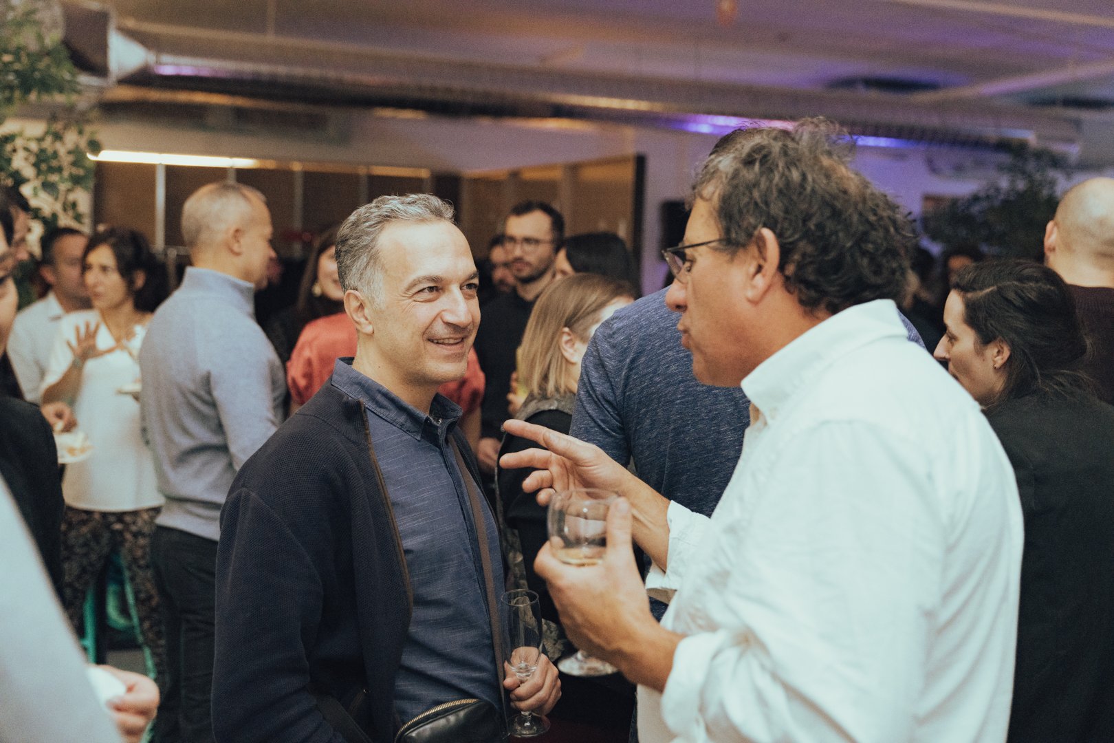 Groupe de personnes en conversation lors d'une réception ou d'une fête, dans un espace intérieur.