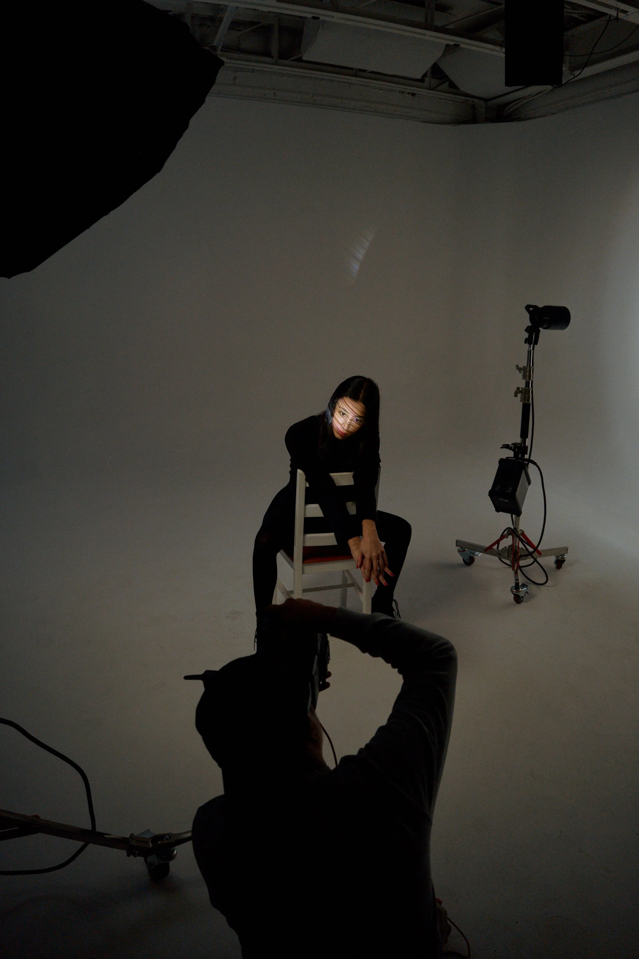 Une femme assise sur une chaise dans un studio photo avec éclairage, en train d'être photographiée par un photographe.