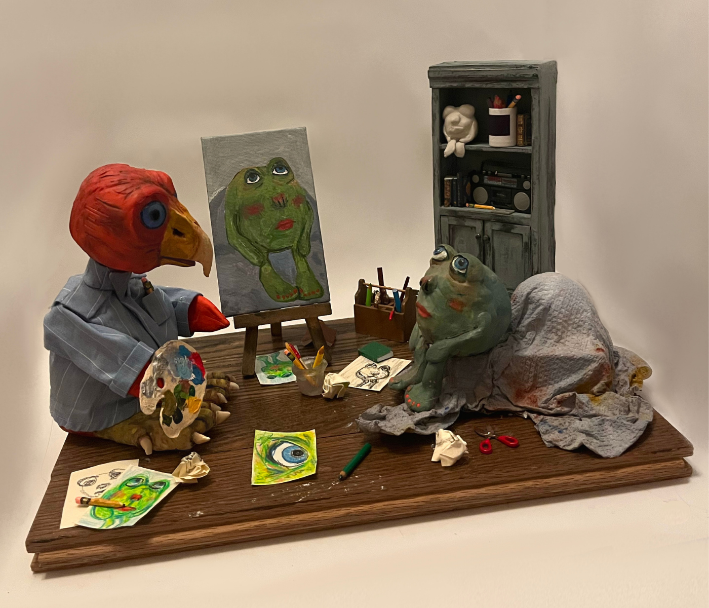 Two creatures in a miniature art studio. The two creatures are green and red.