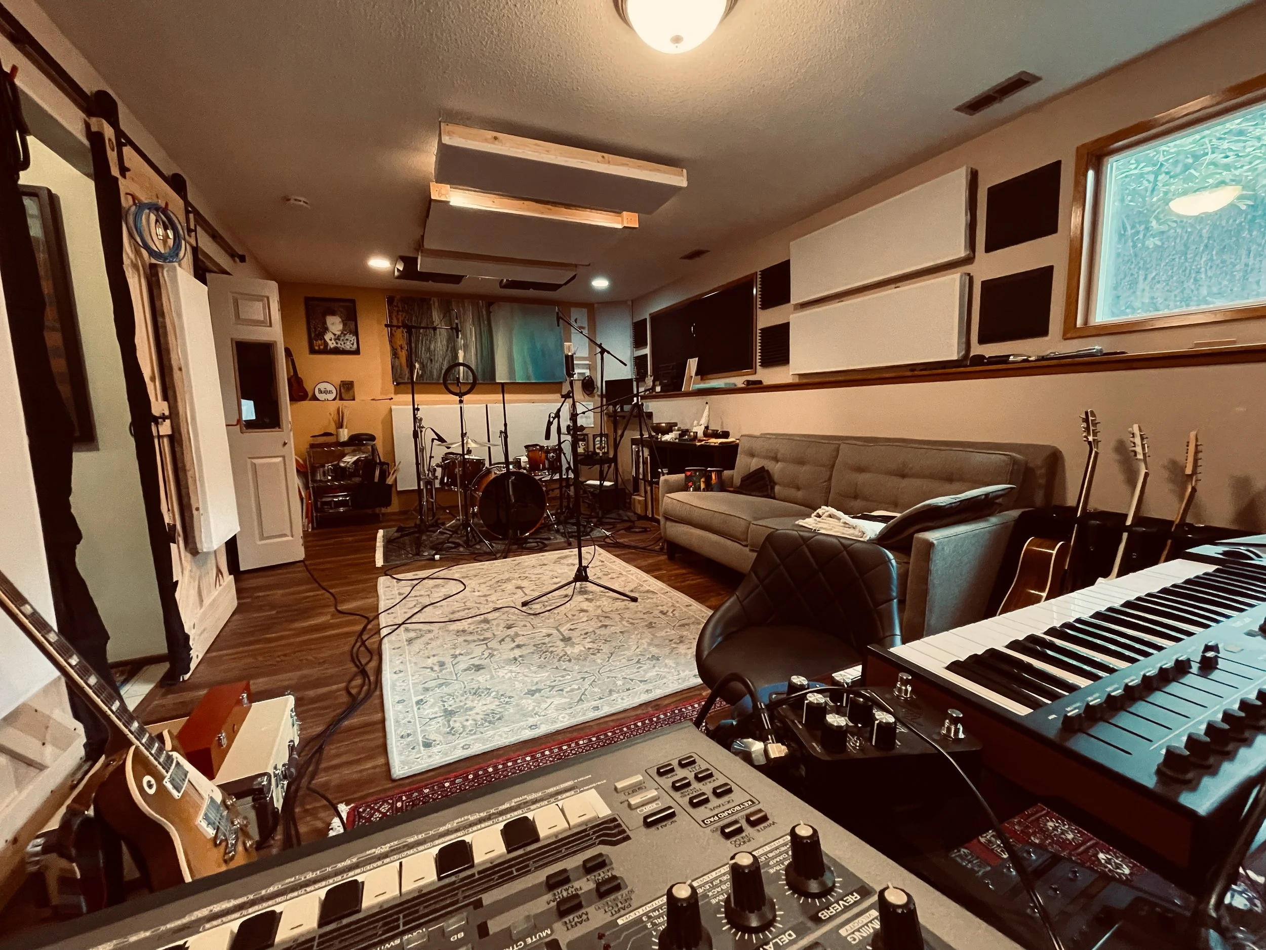 Home recording studio with musical instruments, including guitars, keyboard, and drum set, soundproofing panels, and audio equipment.