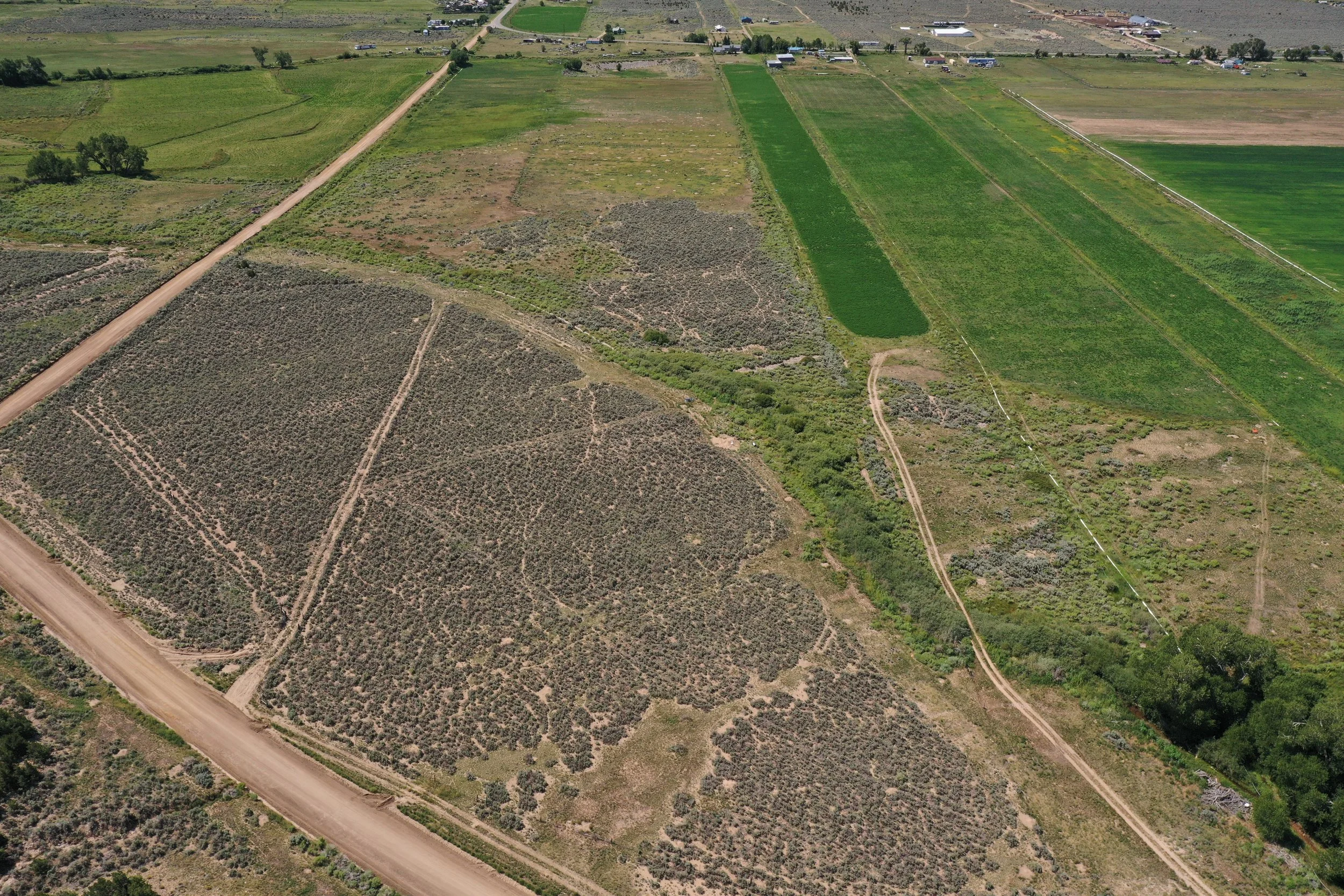 Aerial view of farmland and rural area with fields, dirt roads, and scattered houses in the distance.