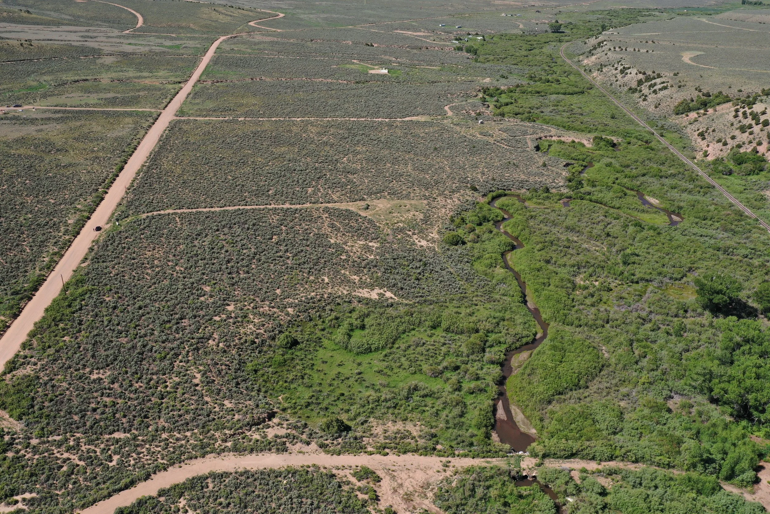 Aerial view of a rural landscape with dirt roads, green vegetation, a winding river, and some small structures.