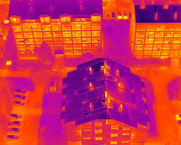 Infrared thermal image of a multi-story residential building with surrounding parking lots and nearby buildings.